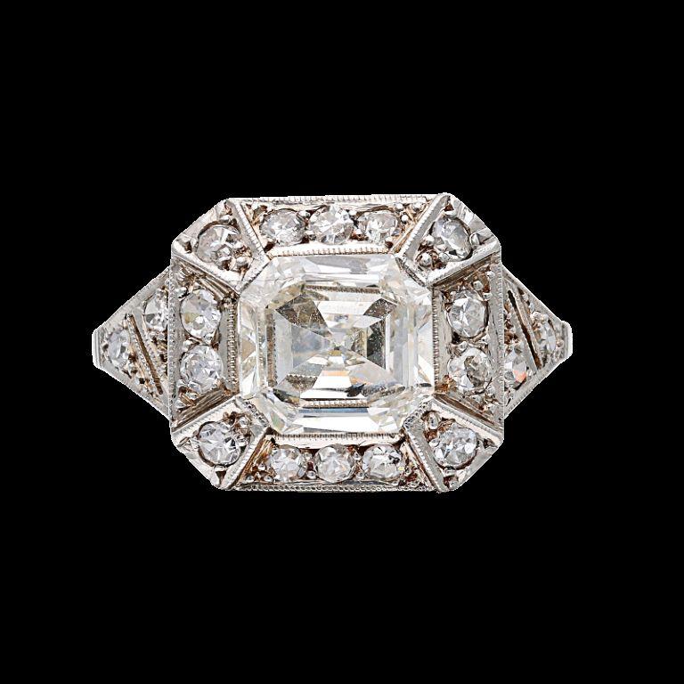 Centering a square emerald cut diamond, accented by 18 single cut diamonds. - Emerald cut diamond weighs approximately 1.40 carats - Single cut diamonds weighing a total of approximately 0.45 carat - Size 6 1/4 - Total weight 3.31 grams - Platinum