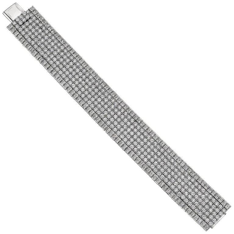 Wide flexible bracelet, featuring a central band composed of five rows of round brilliant-cut diamonds flanked by a single row of princess-cut diamonds on either side, made of platinum.
 
305 round brilliant-cut diamonds weighing ~28.27 total carats