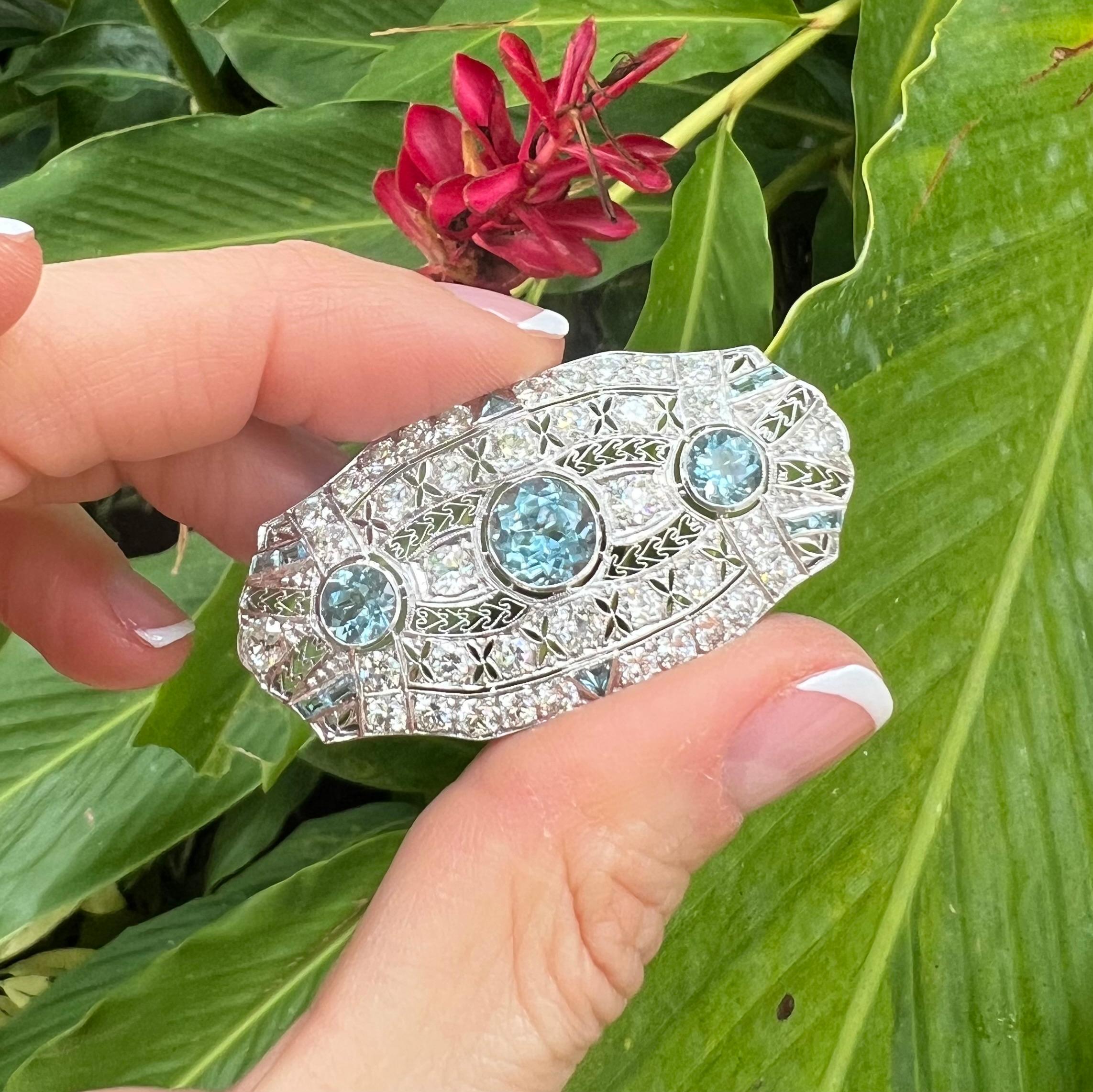 Aquamarine, diamond and platinum brooch from the Edwardian period.  The beautiful handcrafted, elongated oval-shaped mounting displays a pierced cut-out design with filigree accents throughout.  Having three central round faceted aquamarines in a