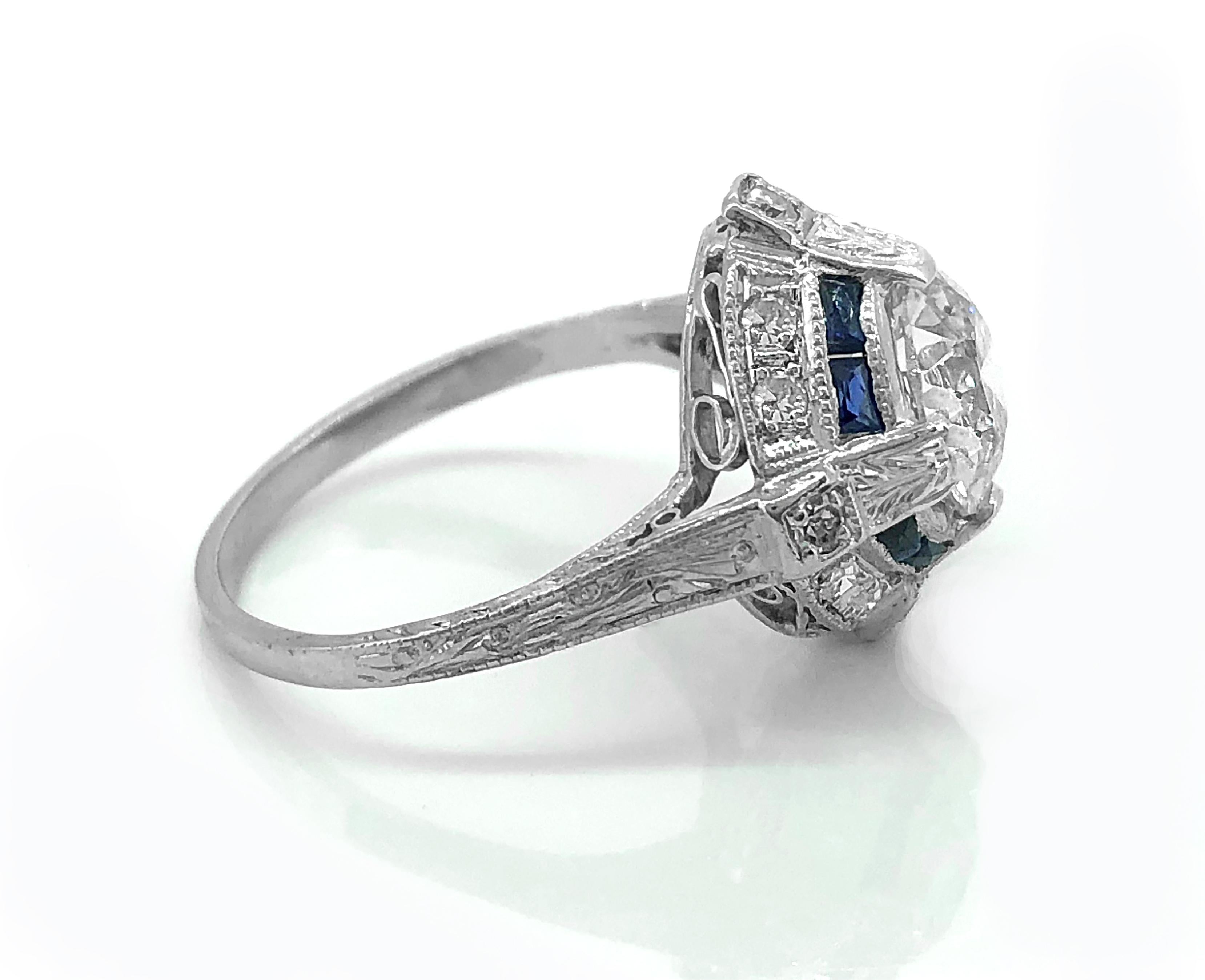 A dazzling Platinum Art Deco diamond Antique engagement ring features a 1.65ct. Apx. European cut diamond with VS2 clarity and J color. The center stone is surrounded by .50ct. T.W. Apx. of baguette cut blue sapphires. Additionally, there are .20ct.