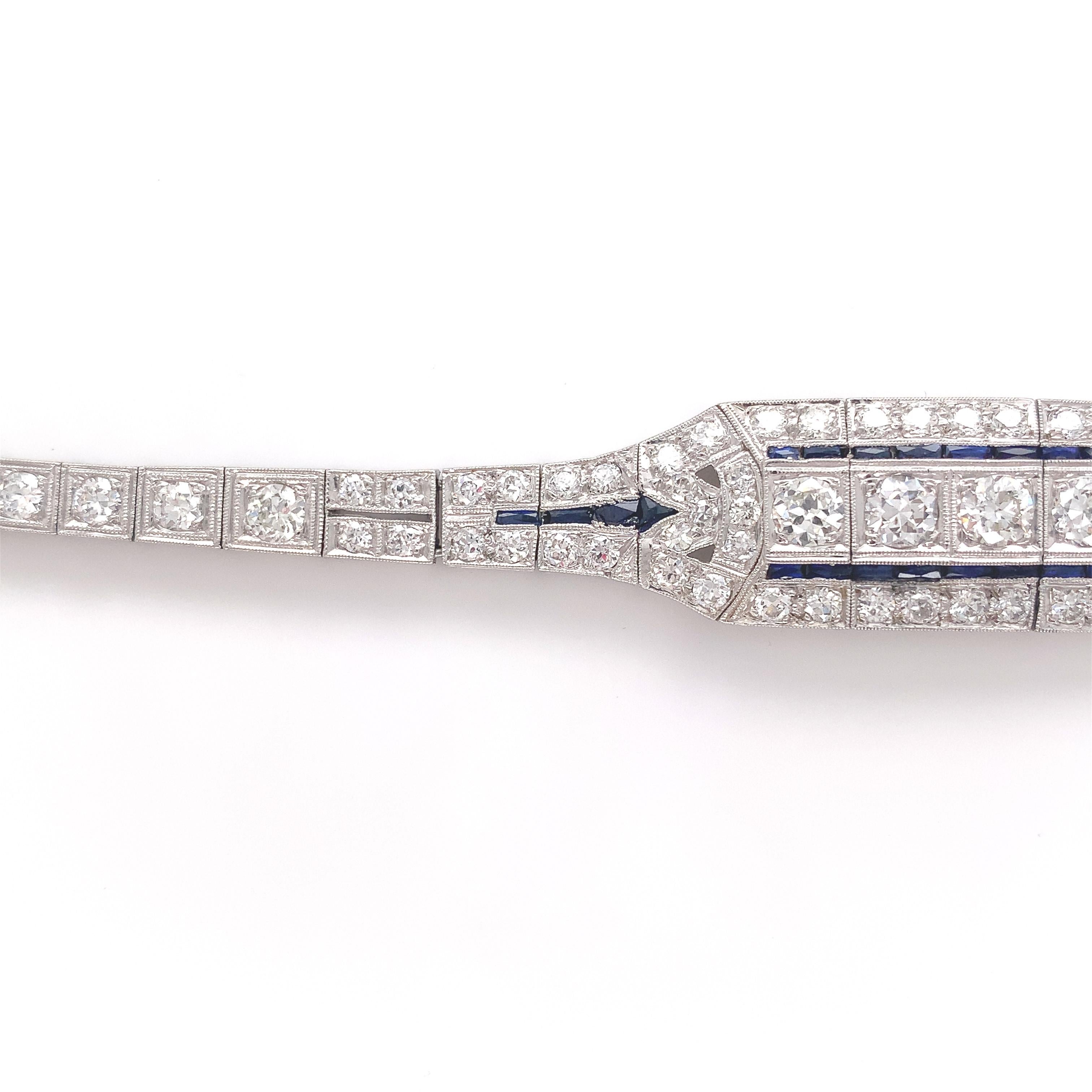 Antique platinum Art Deco diamond bracelet featuring about 4.25 carats of diamonds accented by calibre cut synthetic blue sapphires. The bracelet has crisp detail with milgrain and piercing. There are a total of 88 diamonds including 4 larger