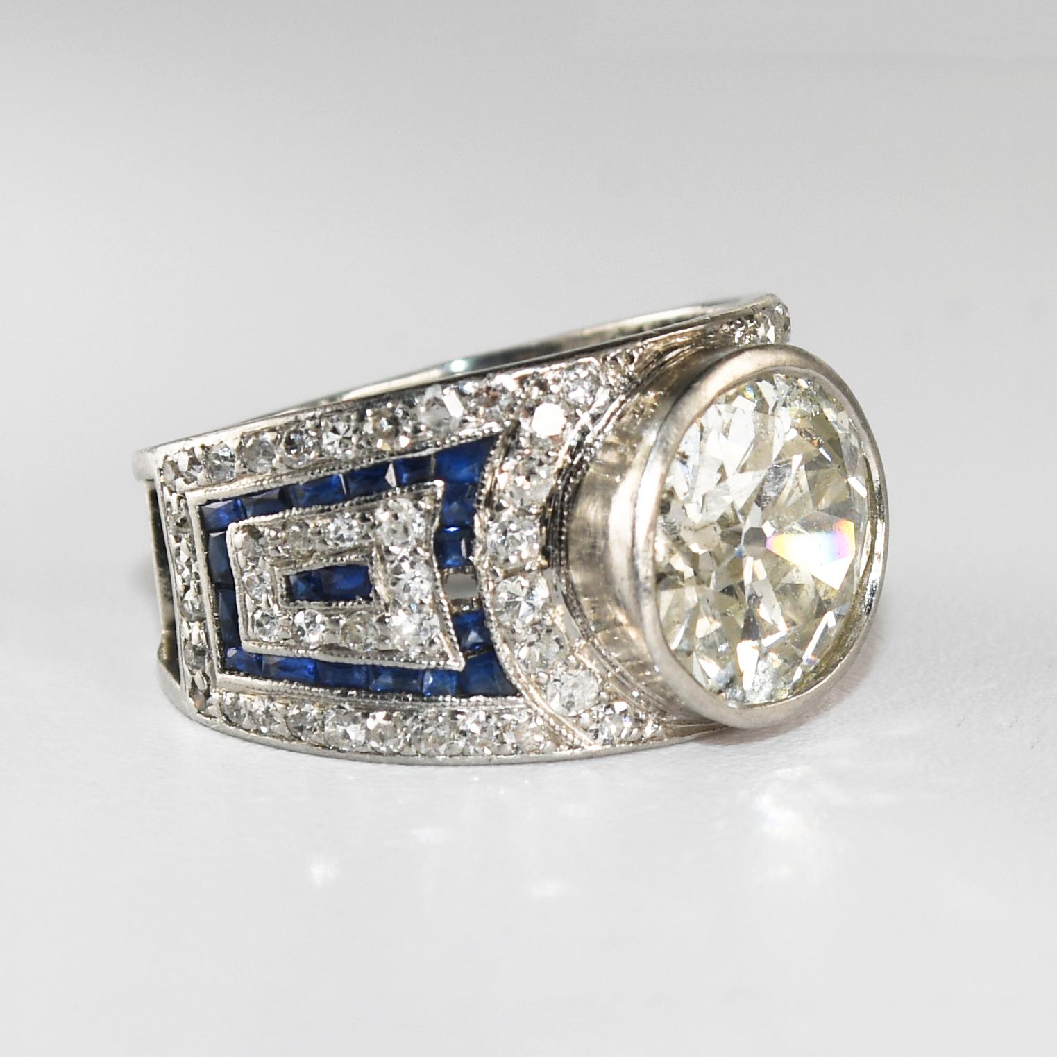 Anello in platino con diamante Art Deco e pietra centrale Old Euro Cut.
Ci sono piccoli accenti di diamanti e uno spinello blu sul gambo. 
È difficile confermarlo viste le dimensioni ridotte delle pietre laterali. 
Ci sono alcuni piccoli diamanti a