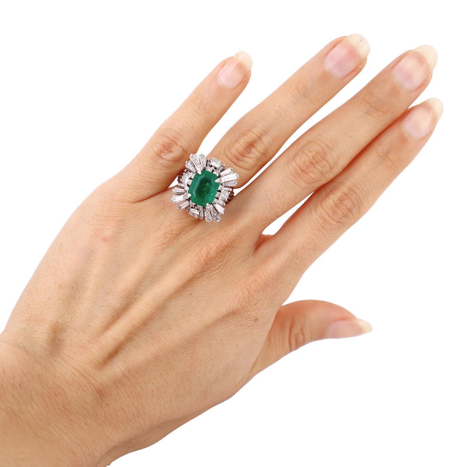 This vintage ballerina ring is masterfully crafted in platinum, featuring a striking center emerald-cut natural emerald of approximately 2.80 carats. The vivid green emerald is surrounded by a dramatic halo of natural round-cut and tapered