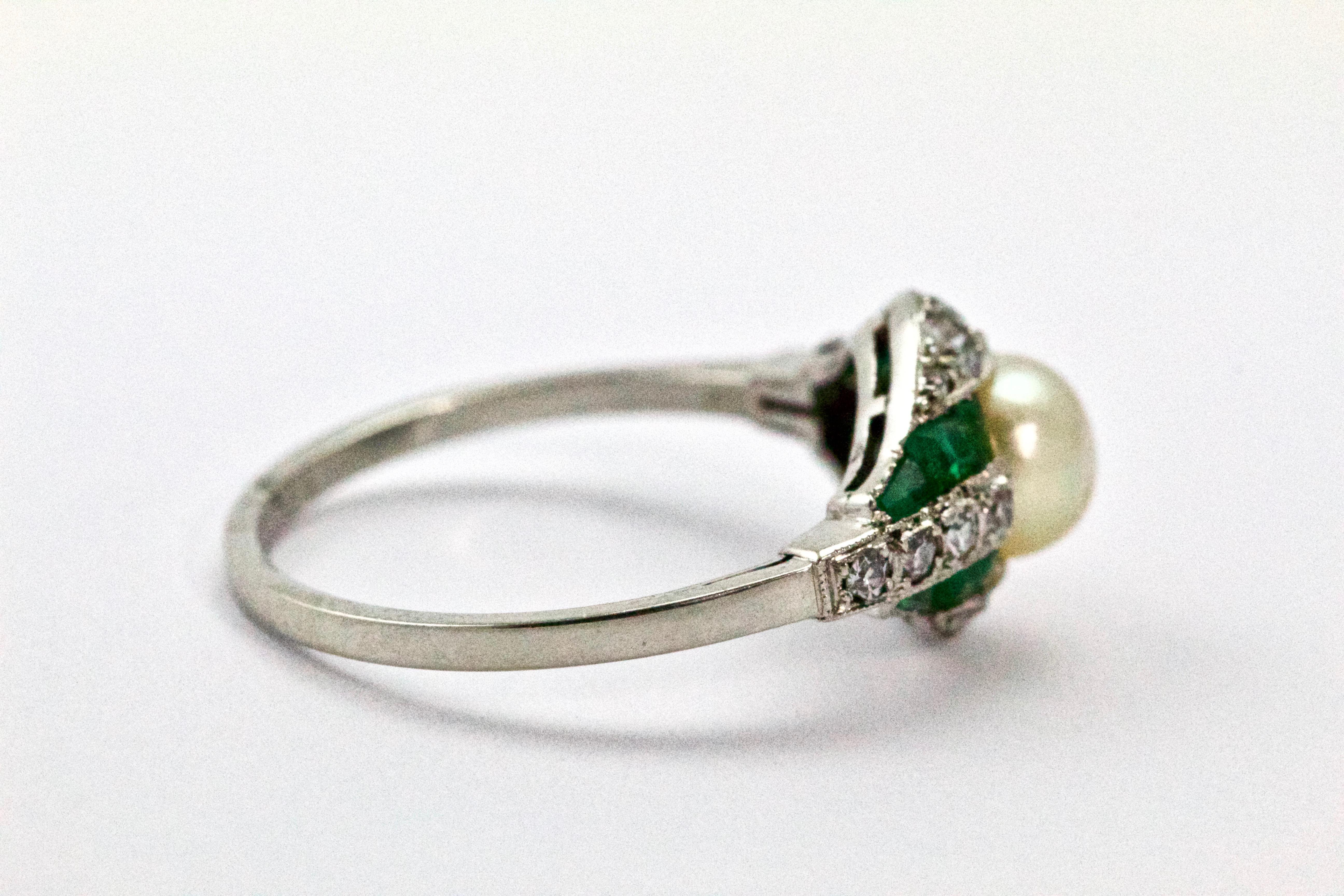 This magnificent Belle Époque ring has a central natural saltwater pearl, ever so slightly off-round with a lovely warm white body color with slight rose overtone it displays wonderful lustre and surface quality, accented with calibre cut emeralds,
