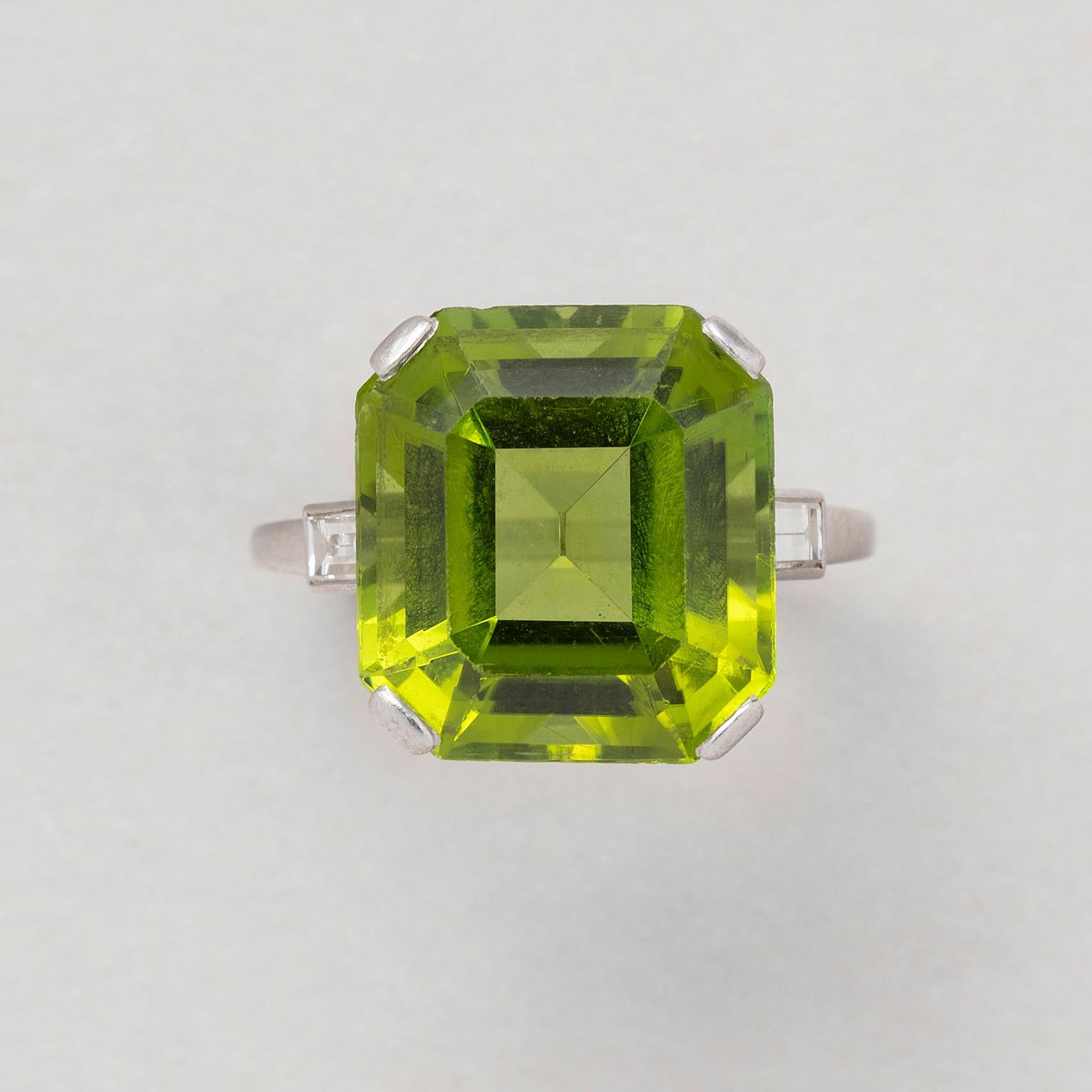 A platinum ring set with a large emerald cut peridot (circa 15 carat) with a small baguette cut diamond on each side, signed and numbered: Cartier, London, 1512.

weight: 6.56 grams
ring size: 17.75 mm / 7 1/2 