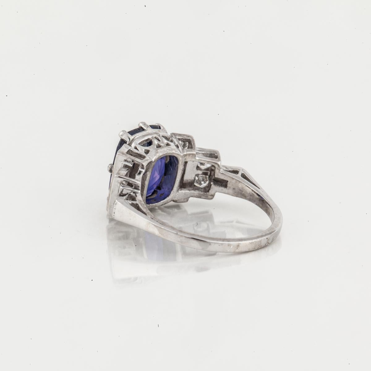 Platinum ring featuring a cushion-cut color changing sapphire accented by diamonds.  The sapphire is a blue/purple Ceylon stone weighing 4.13, natural and unheated, accompanied by an AGL certificate.  There are 12 round diamonds totaling 1 carat;