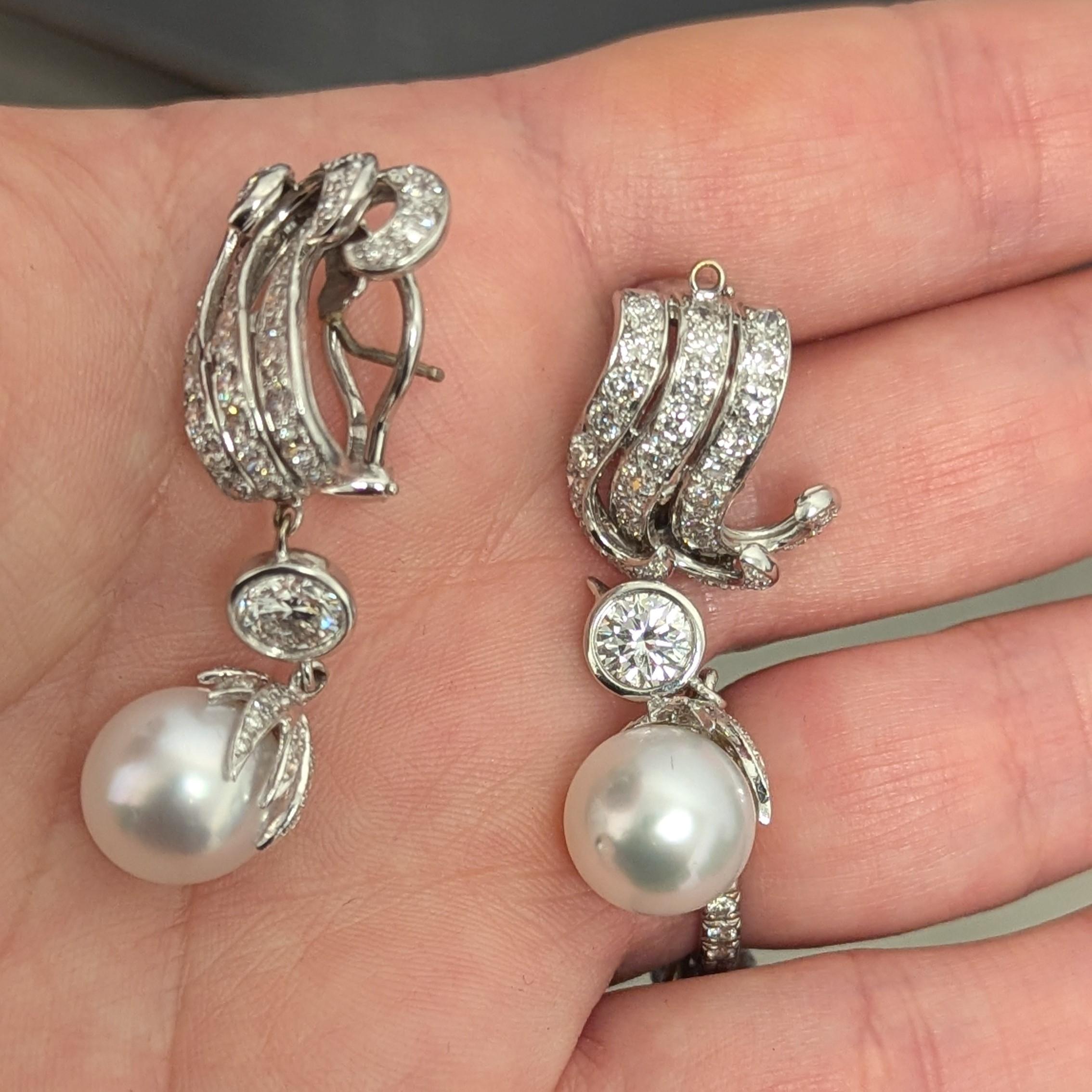 These intricately designed pearl drop earrings feature two larger diamonds, weighing approximately 1.75cts, with a G-H color range and SI clarity, surrounded by round diamonds, mostly H-I VS-SI, and accented with two dangling pearls. 