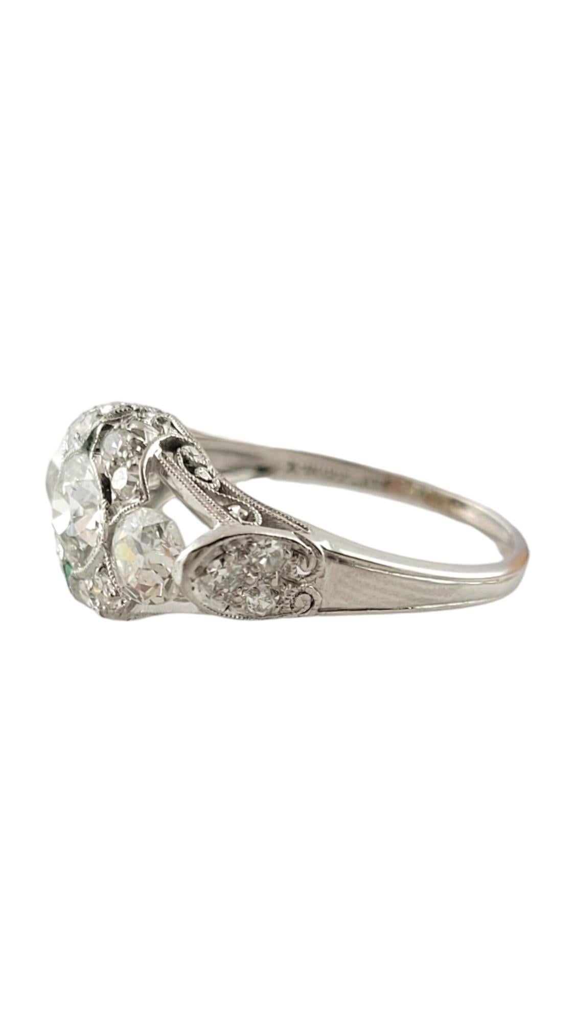 This sparkling ring features one round brilliant cut diamond in its center (.62 ct.) accented with 16 round brilliant cut diamonds and two natural trillion cut emeralds set in beautifully detailed platinum.  

Width:  10 mm.  Shank:  1.5 mm.

Total