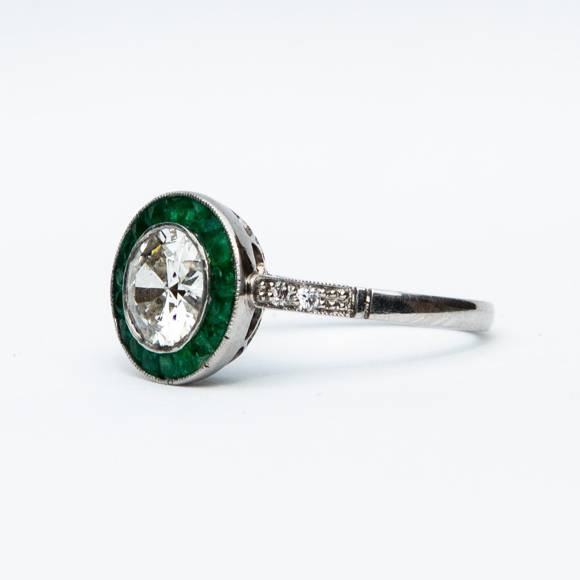 A beautiful example of a platinum emerald and diamond target ring. The central diamond measures 1 carat 30 and is surrounded by emeralds with diamond shoulders to the shank. Total diamond weight certified 1.75 carat, colour I and clarity