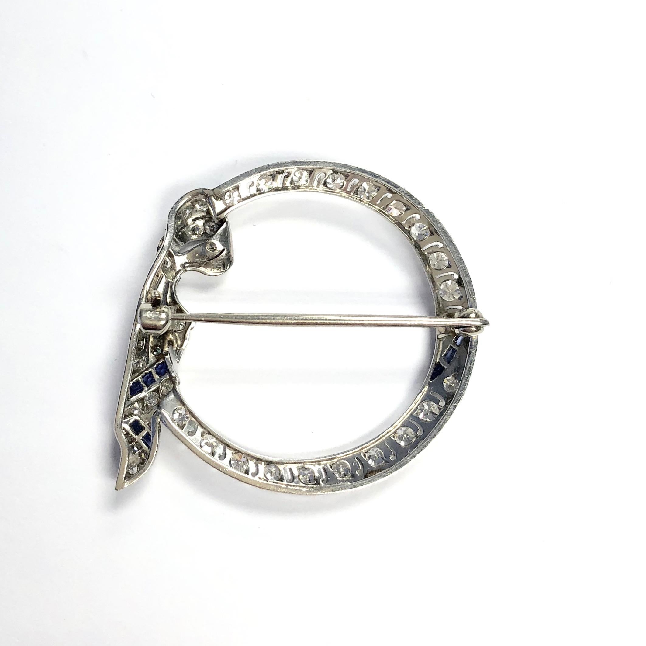Classic Platinum Art Deco circle ribbon brooch set with 43 old european and single cut diamonds and calibre cut sapphire accents.
Approximate total diamond weight: 1.00ct. Color: G-H, Clarity: VS1-VS2
The pin measures 1 3/16 