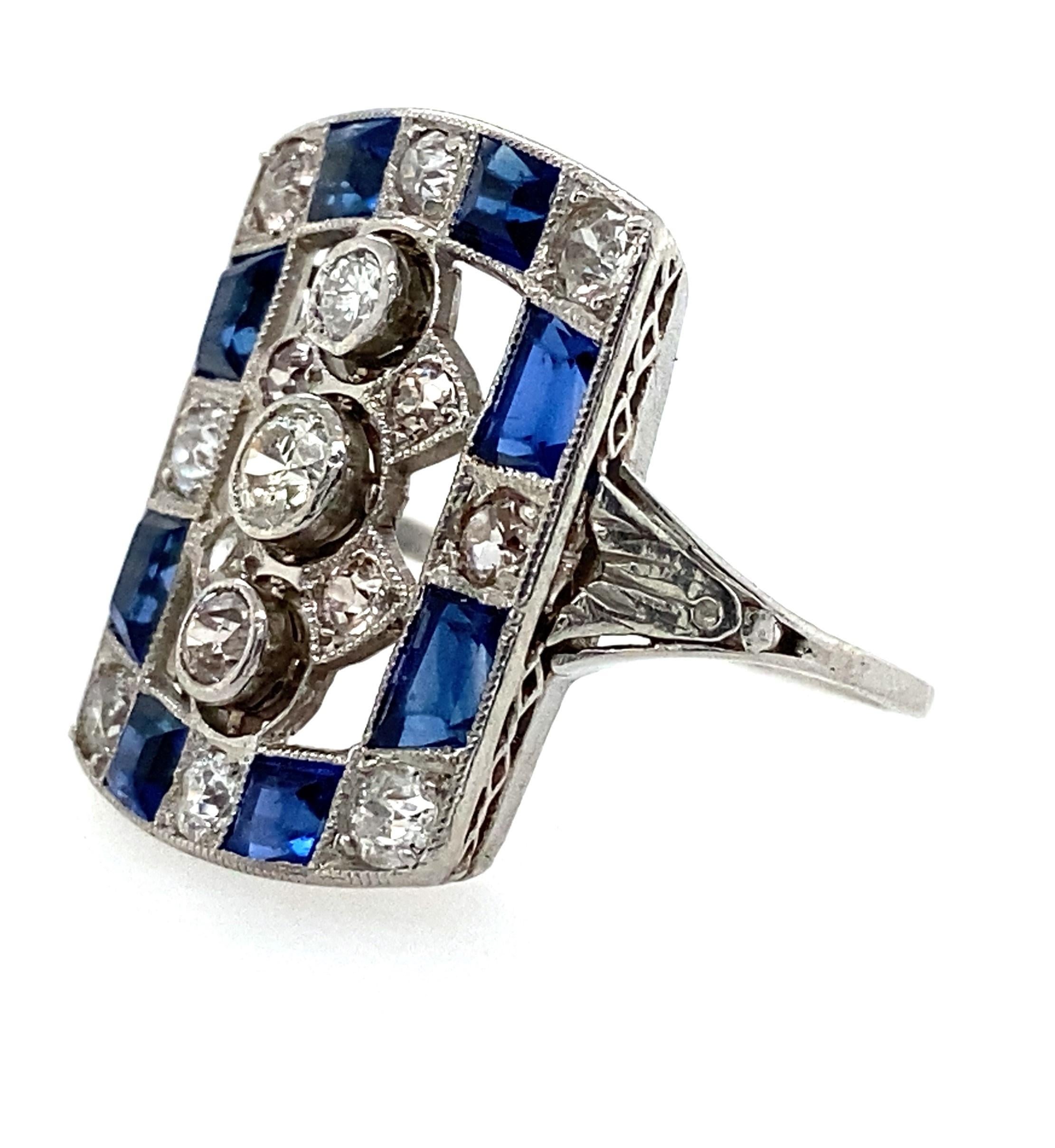 This platinum Art Deco ring is absolutely stunning. A checkerboard pattern of diamond and brilliant blue lab-grown sapphires surround a row of three bezel set old European cut diamonds and four smaller diamonds set in between them. The engraved