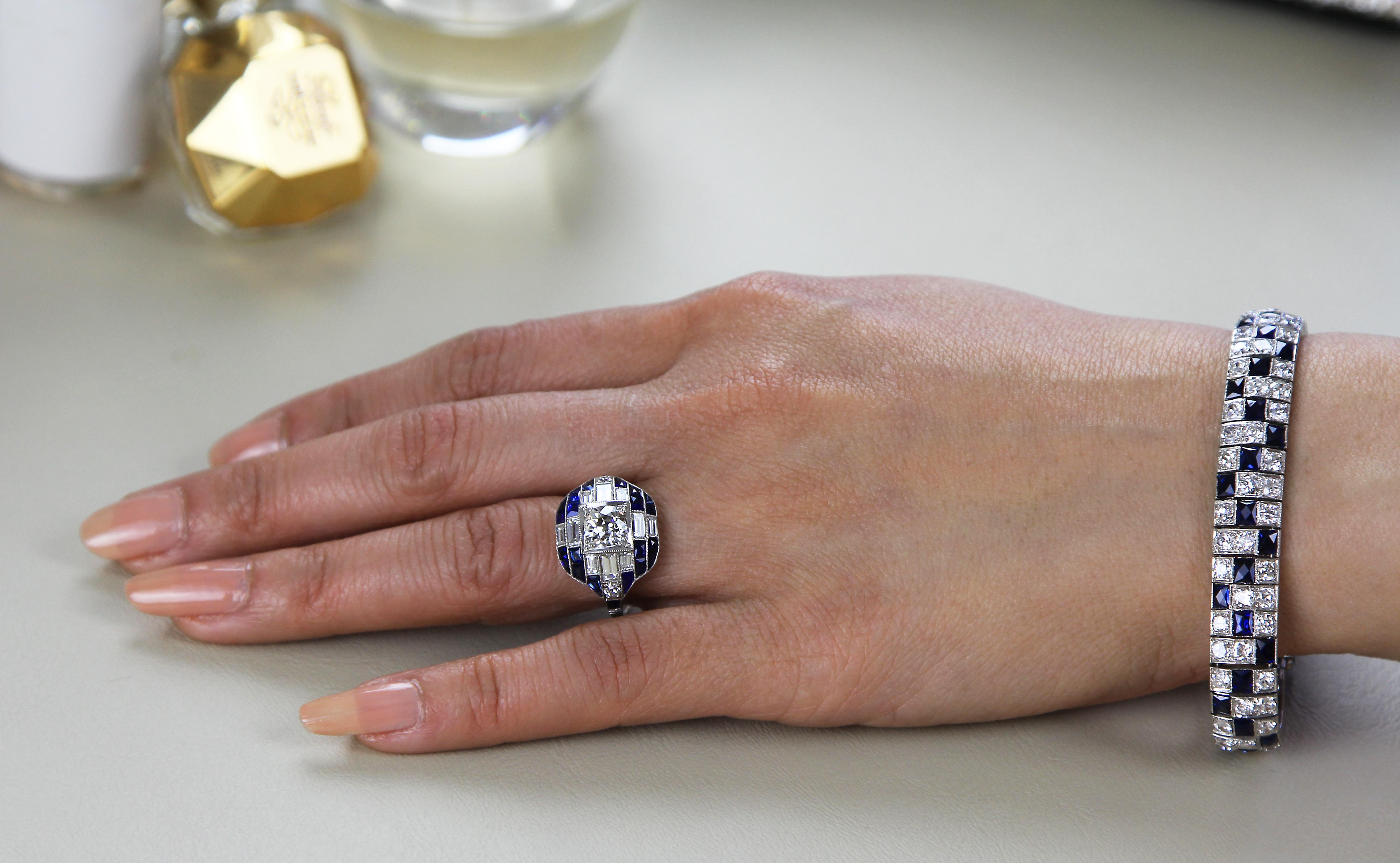 An Art-Deco style, diamond and sapphire cocktail ring set in platinum. The central old-European-cut diamond is surrounded by baguette-cut diamonds and sapphires, circa 1960's. Its detailed design consists of a bold glistening white round brilliant