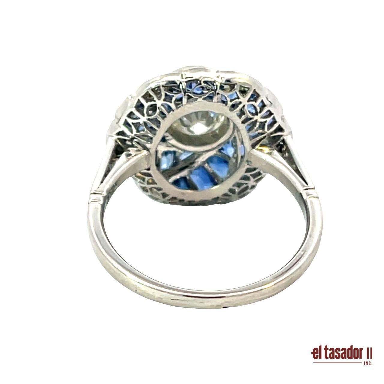 Questo splendido anello in platino è una creazione artigianale con un elegante motivo a vortice e pesa 5,6 grammi. Al centro si trova un diamante taglio brillante di 0,66 carati, circondato da 6,02 carati di vividi zaffiri blu meticolosamente