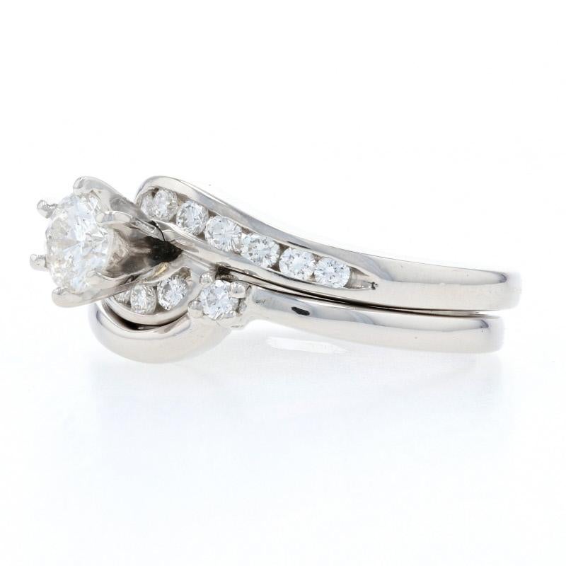 Erfüllen Sie sich die Träume Ihrer Liebsten mit diesem atemberaubenden Brautset! Dieser aus Platin gefertigte Verlobungsring im anmutigen Bypass-Stil zeigt einen strahlenden Diamantsolitär:: der von funkelnden Diamantakzenten um den Mittelstein