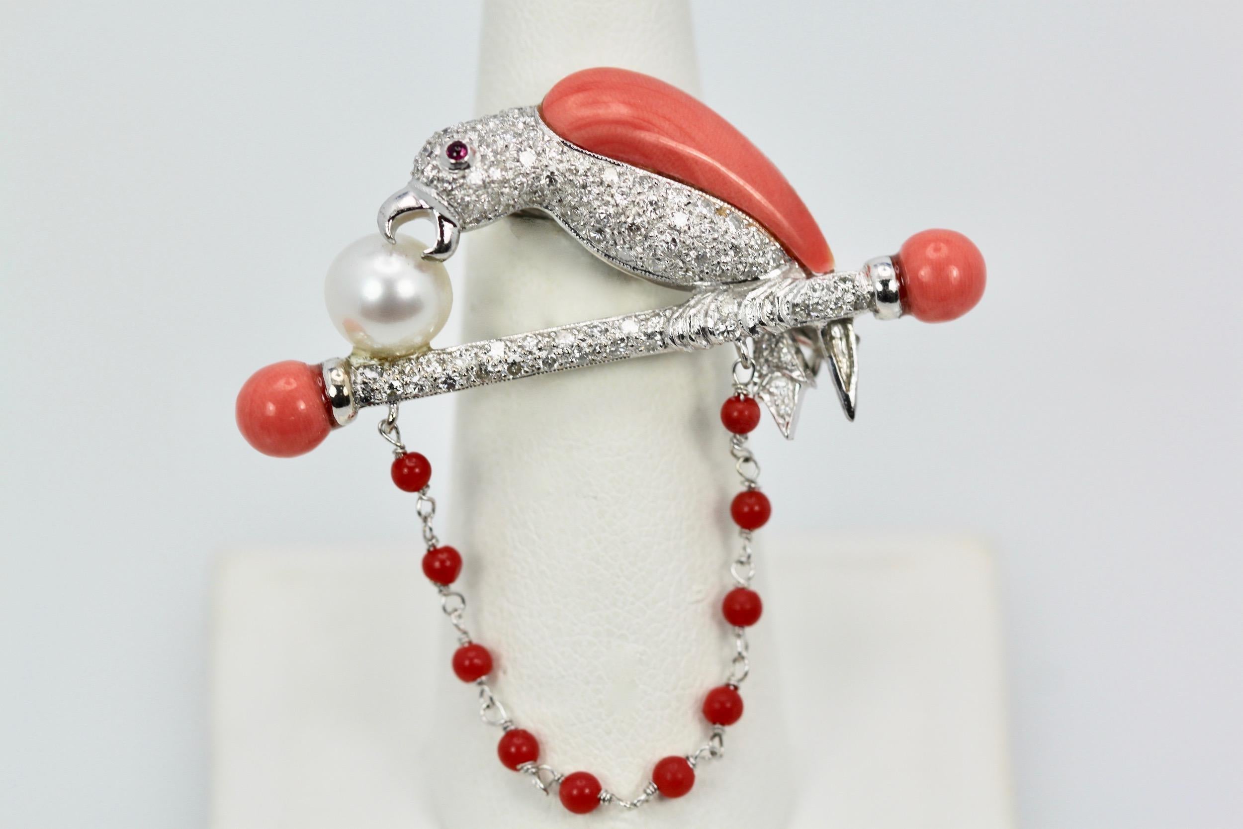 Platinum Diamond Coral Pearl Parrot Brooch on Bar Branch is a gorgeous bird pin featuring a parrot made of fine coral and diamonds. This parrot sits on a branch with coral terminals and a pearl sitting on the bar. It further has a coral beaded chain