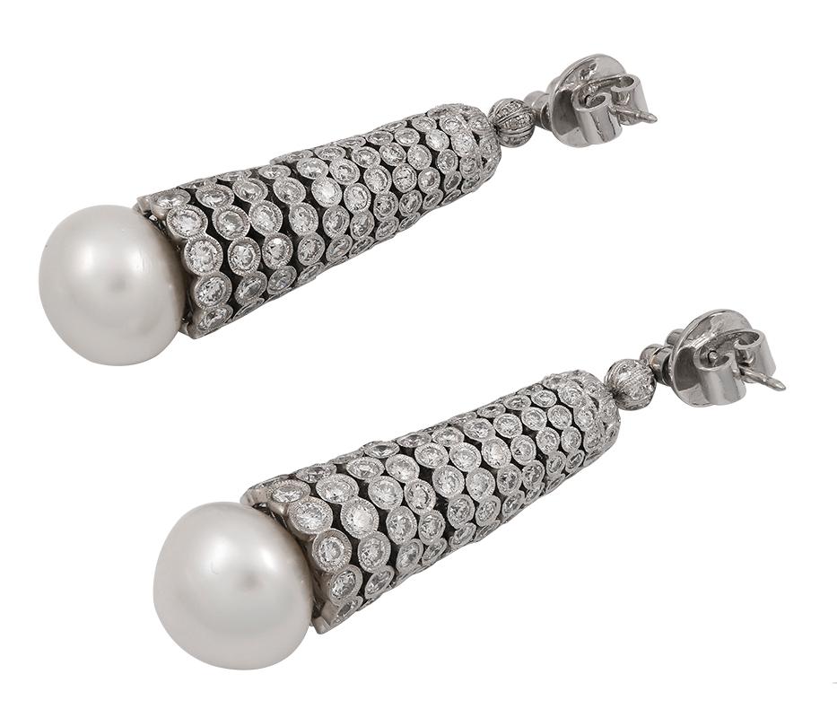 Elegant platinum, pearl and diamond drop earrings designed as two small bezel-set diamonds with post fittings above diamond-set beads and caps suspending flexible, graduated cylinders of 11 round diamond discs above large white button-shaped