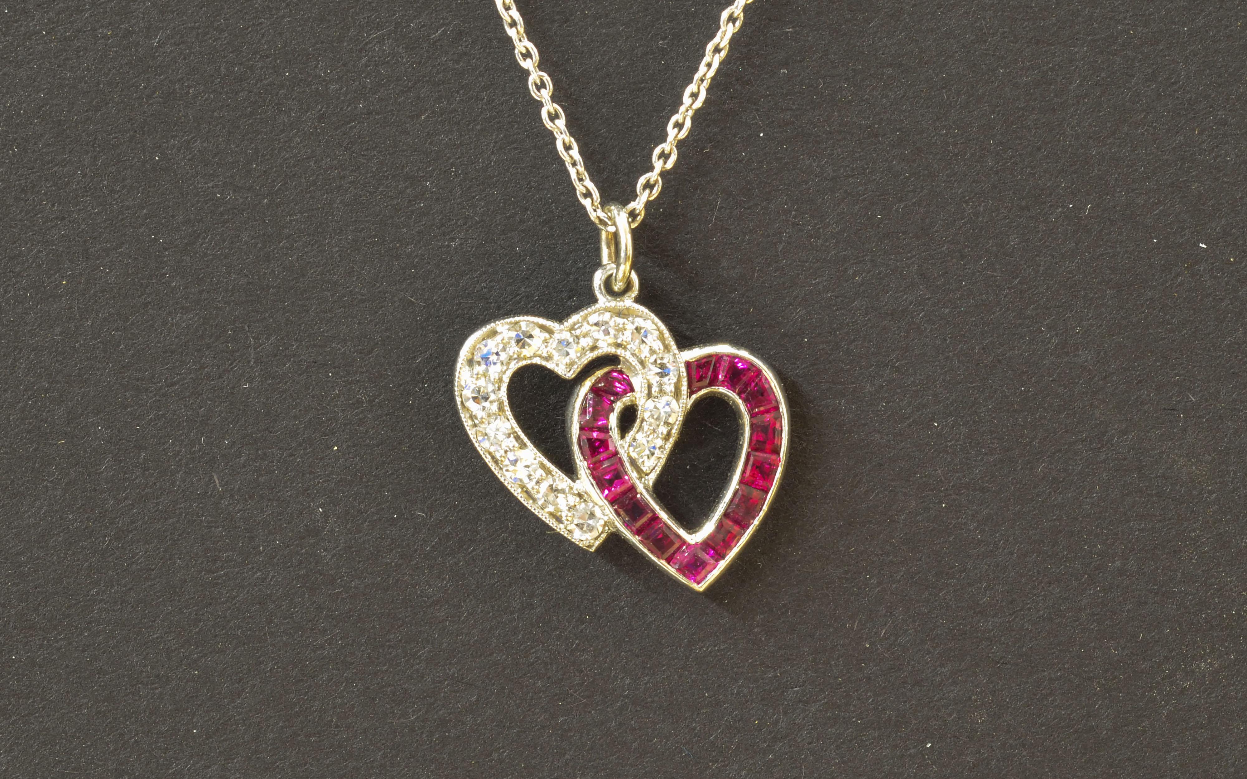 Very pretty double heart Platinum pendant, set with 14 single cut Diamonds and 14 calibre cut fine Rubies. It hangs from a 18K white gold chain 16 inches long. It is signed 