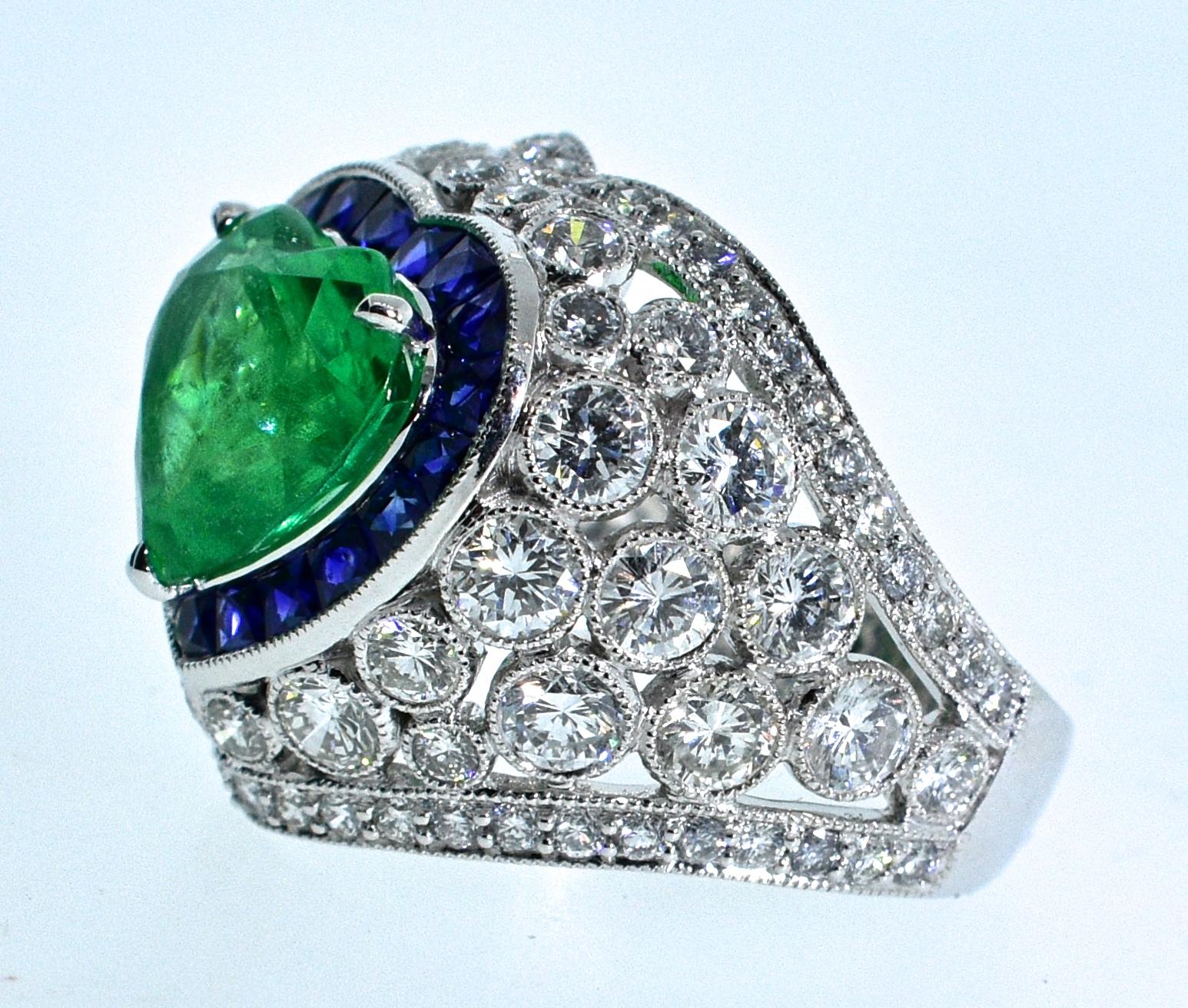 Emerald, sapphire, diamond and platinum ring, the center heart shaped emerald certified to be natural Colombian.  The emerald weighs 3.2 cts, exactly.  
There are 19 French cut natural bright blue sapphires, weighing .99 cts.  There are 3.06 cts.,
