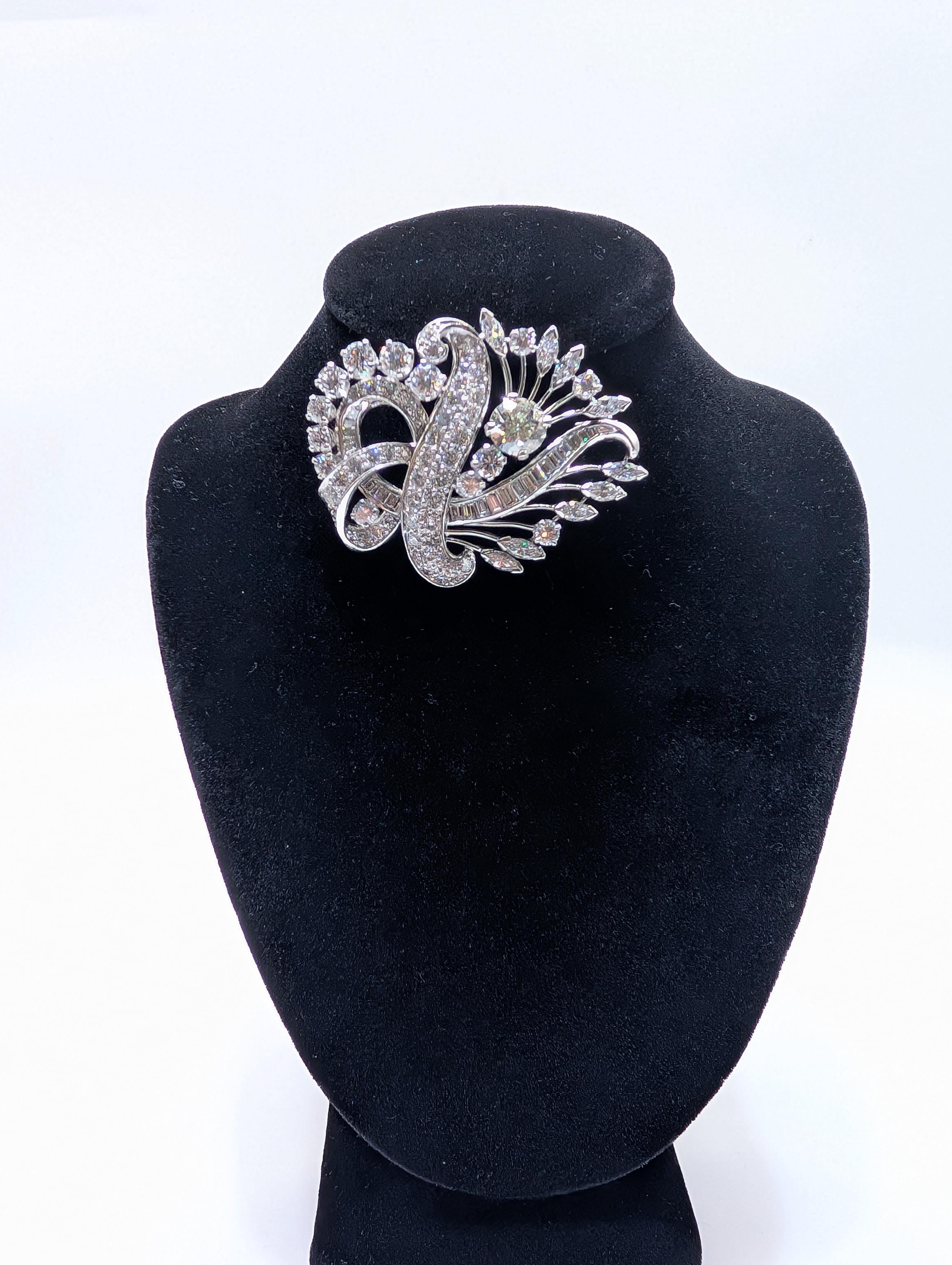 Questa spilla è uno splendido pezzo di alta gioielleria realizzato in platino e tempestato di diamanti. L'intricato design presenta un motivo grazioso e fluente che combina con eleganza vari tagli di diamanti. Il fulcro centrale è costituito da un