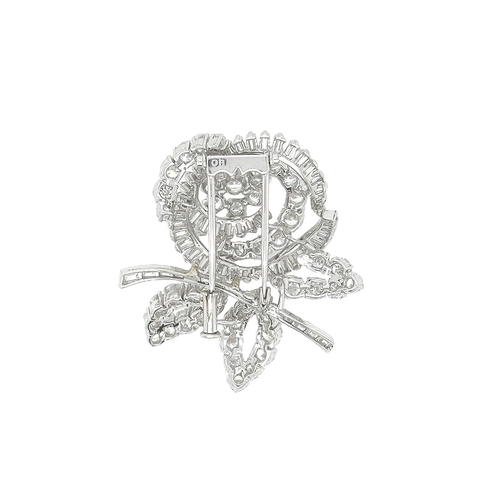 A platinum and diamond brooch.  Designed in a floral and foliate motif, set with approximately 45 baguette cut diamonds and 49 round brilliant cut diamonds.  Total diamond weight approximately 9.45 carats.  Length approximately 1 5/8 inches.  Gross