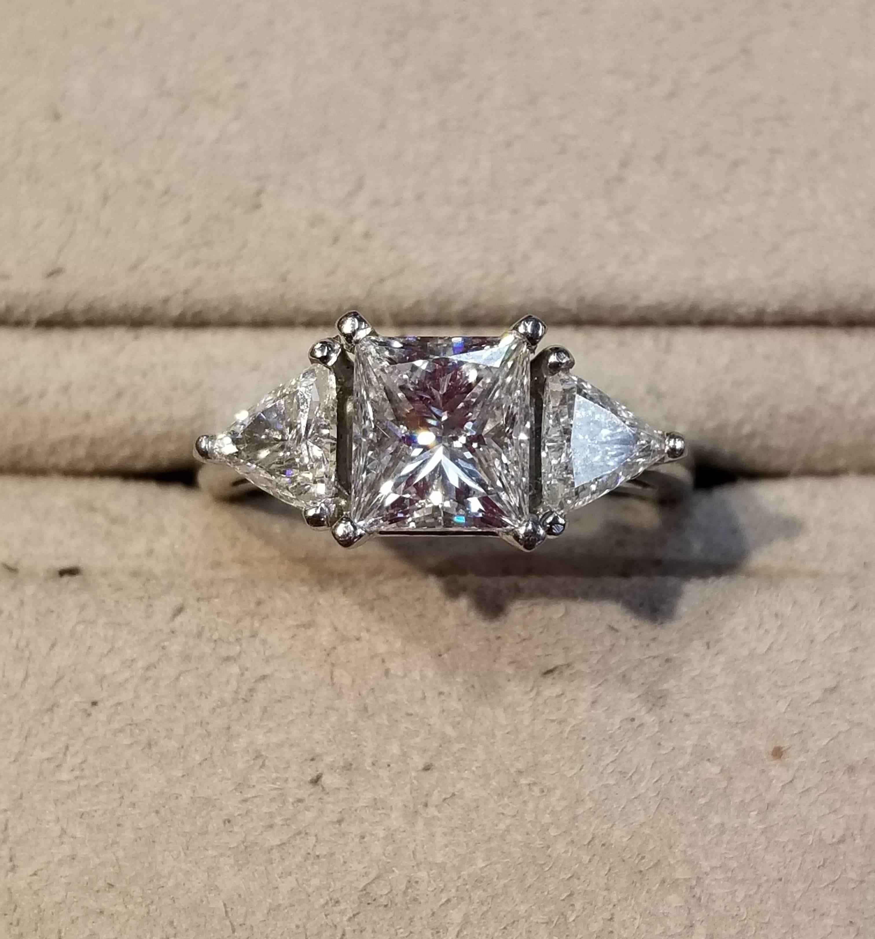 Platinum ring, size 5, with rectangular modern brilliant center stone and two bordering trilliants. The center stone is 1.51 carats, is G color and VVS2 clarity. The trilliants have a combined weight of 0.58 carats are G color.