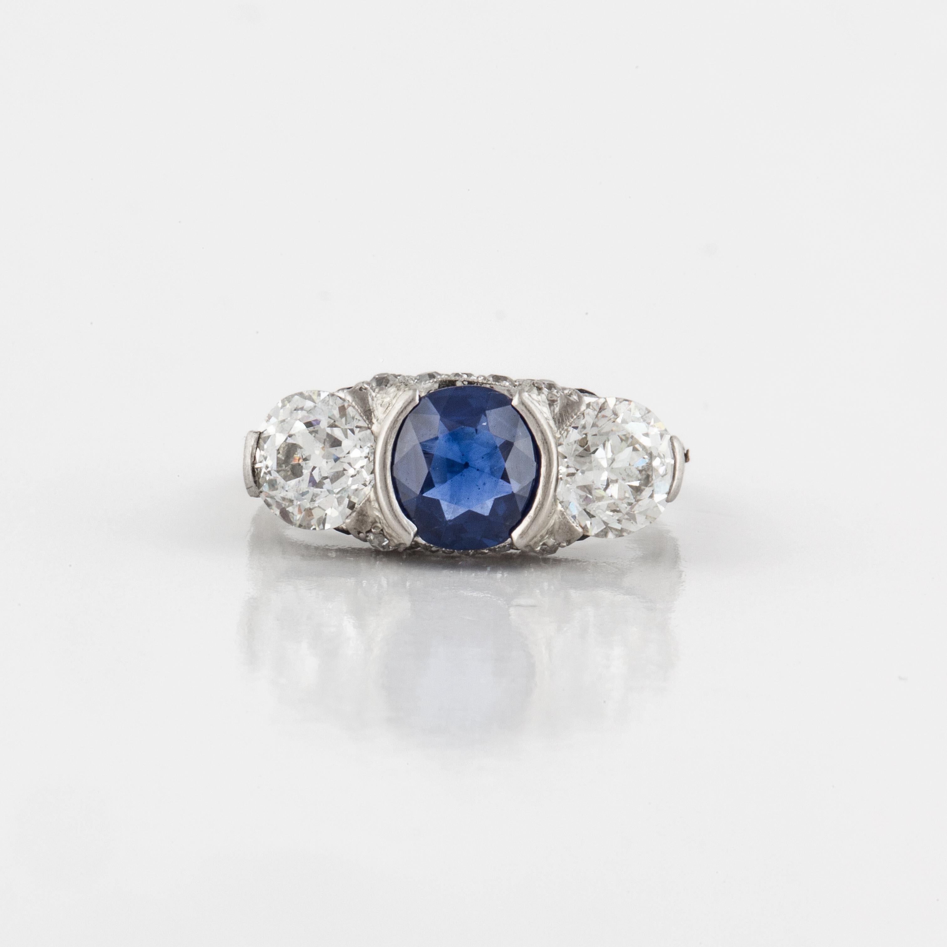 Art Deco three-stone ring in platinum with diamonds and a sapphire. There is one round sapphire weighing 1.18 carats, natural, no heat, Cambodian (Pailin), with an AGL Certificate.  The two side diamonds are old European cuts totaling 1.25 carats;