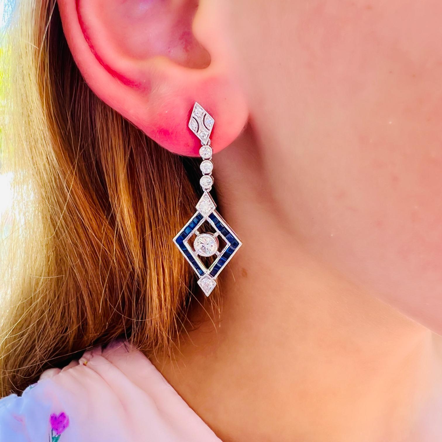 Art Deco style meets incredibly fine materials in these gorgeous diamond and sapphire drop earrings. At the center of this beautiful pair are two sparkling natural white diamonds weighing a total of 0.48 carats (G/VS), surrounded by a diamond design