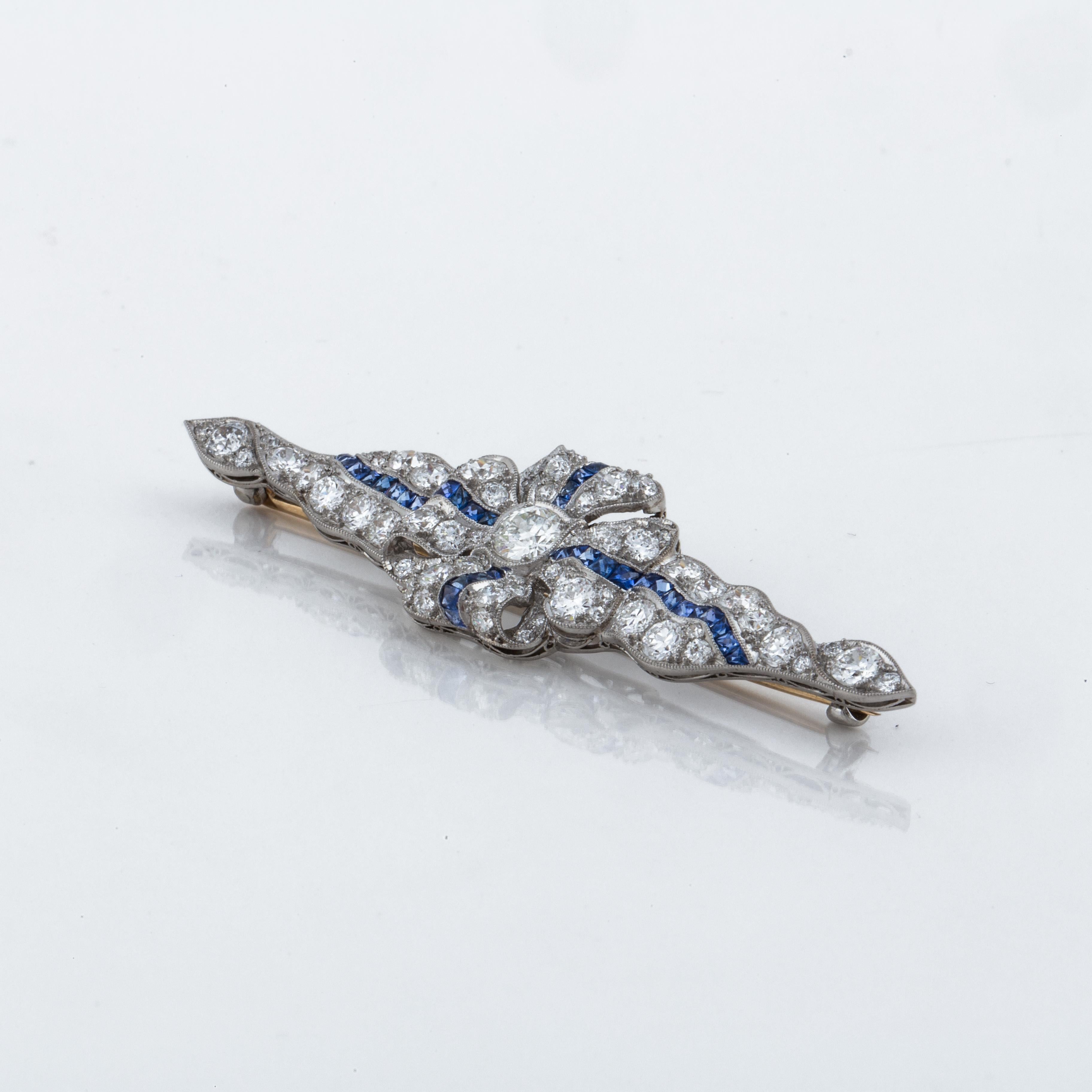 Platinum pin with an 18K yellow gold stem in a ribbon motif.  There are 38 square-cut sapphires and 65 round diamonds totaling 5 carats; H-I color and VS1-VS2 clarity.  Pin measures 2 5/8 inches long and 3/4 inches wide.  Closure is a 