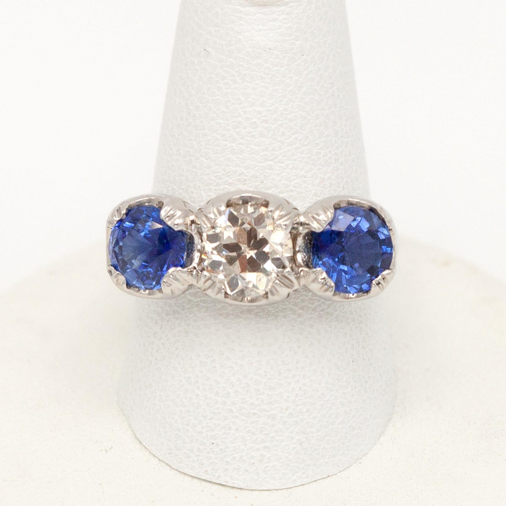 Cette magnifique bague à trois pierres exquise en platine, sertie d'un diamant de taille européenne ancienne d'environ 1,40 carats de couleur I et de pureté SI, flanqué de deux saphirs bleus naturels bien assortis d'environ 1,04 carats et 1,22