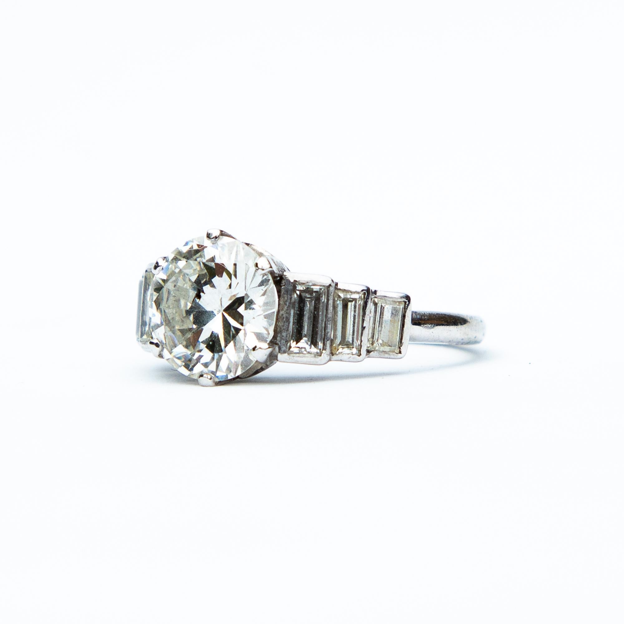 This a stunning Art Deco inspired solitaire platinum and diamond ring. The central modern brilliant cut diamond is beautifully complimented with baguette cut diamond stepped shoulders. There is one small inclusion to the top of the central stone.