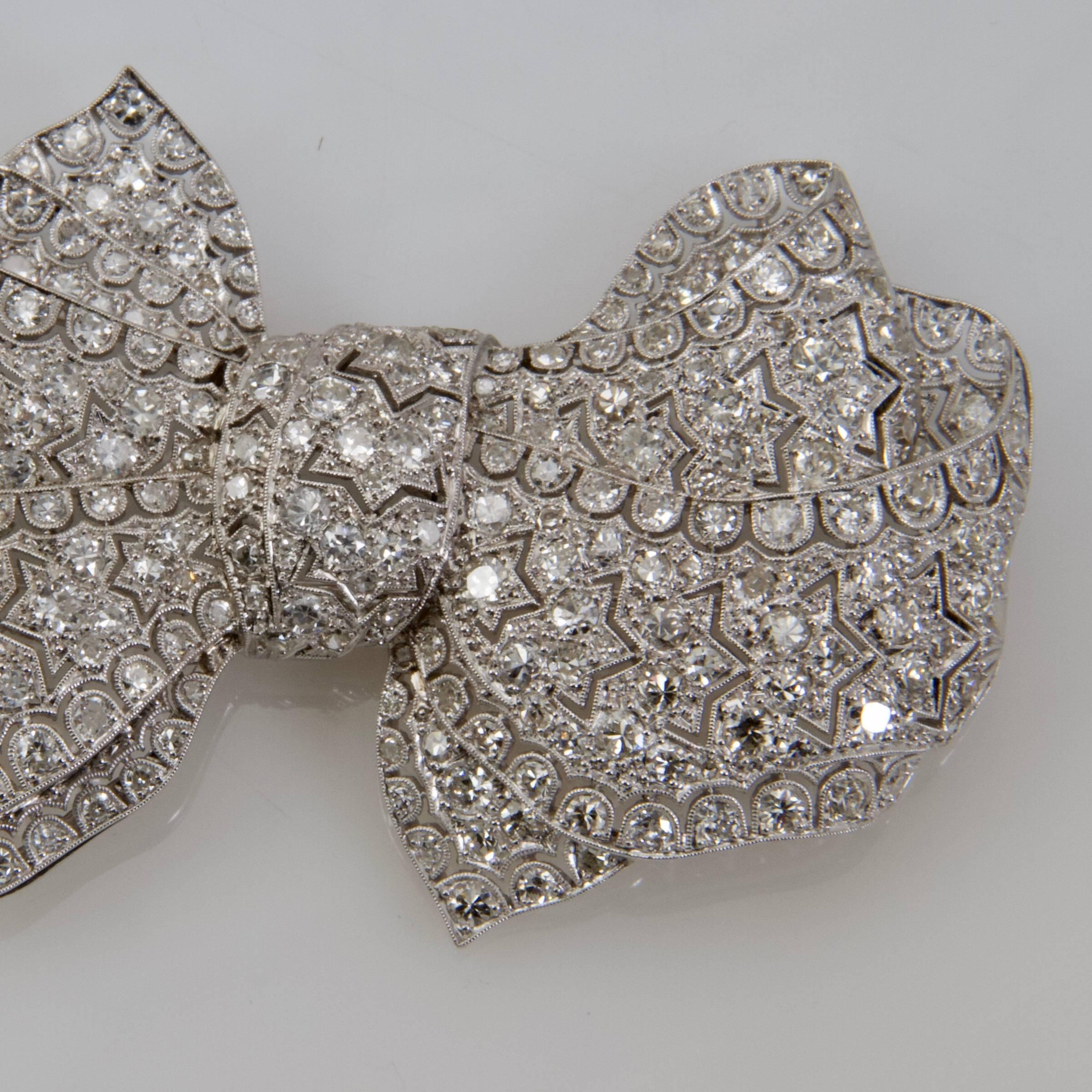 Platinum laced bow brooch set with round diamonds on a ground  decorated with stars and swags. 
Totally bordered with millegrain setting. 
Hoop for a pendant. 
Security system. 
French assays mark.
Maker's mark illegible.
