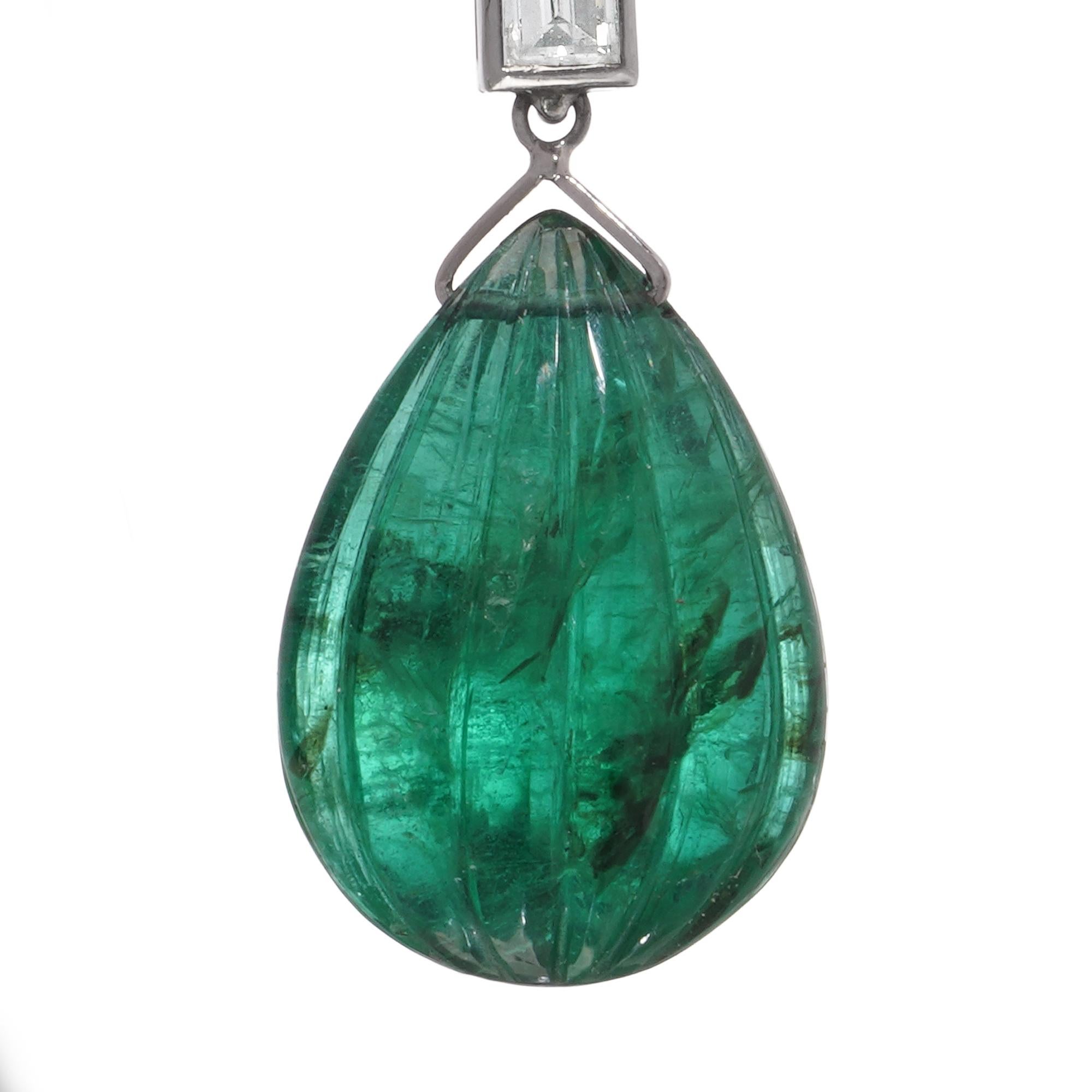 A refined pair of platinum drop earrings, showcasing exquisitely carved emerald cabochons weighing approximately 18.25 carats in total. Each emerald, cut in an elongated drop shape (approx. 20 x 13 mm), is finely fluted and suspended from a