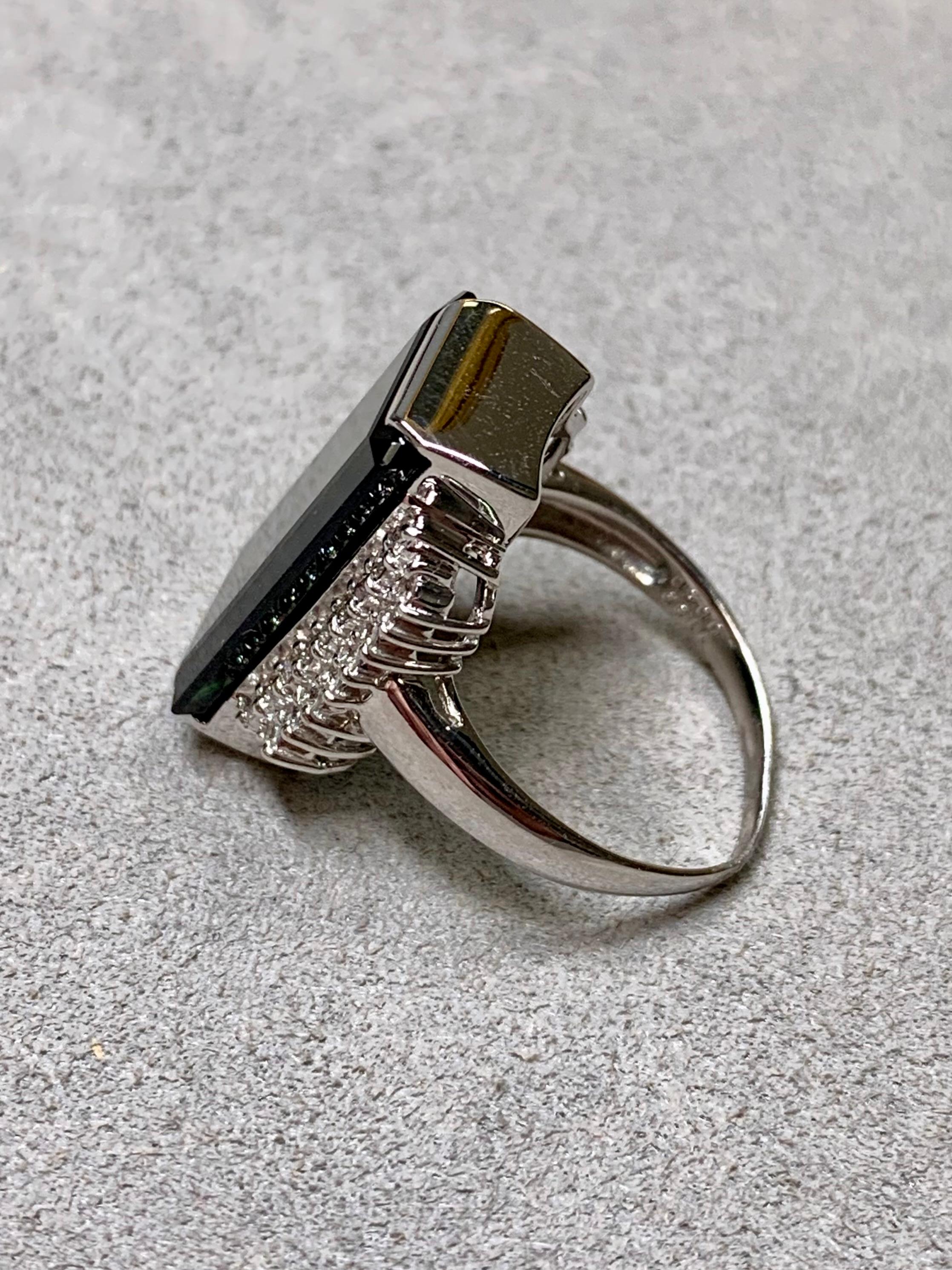 
Cette extraordinaire bague de cocktail en platine met en valeur une tourmaline verte naturelle de 11,86 carats d'une saturation et d'une clarté remarquables. La taille en escalier allongée souligne la profondeur fascinante de la pierre et son éclat