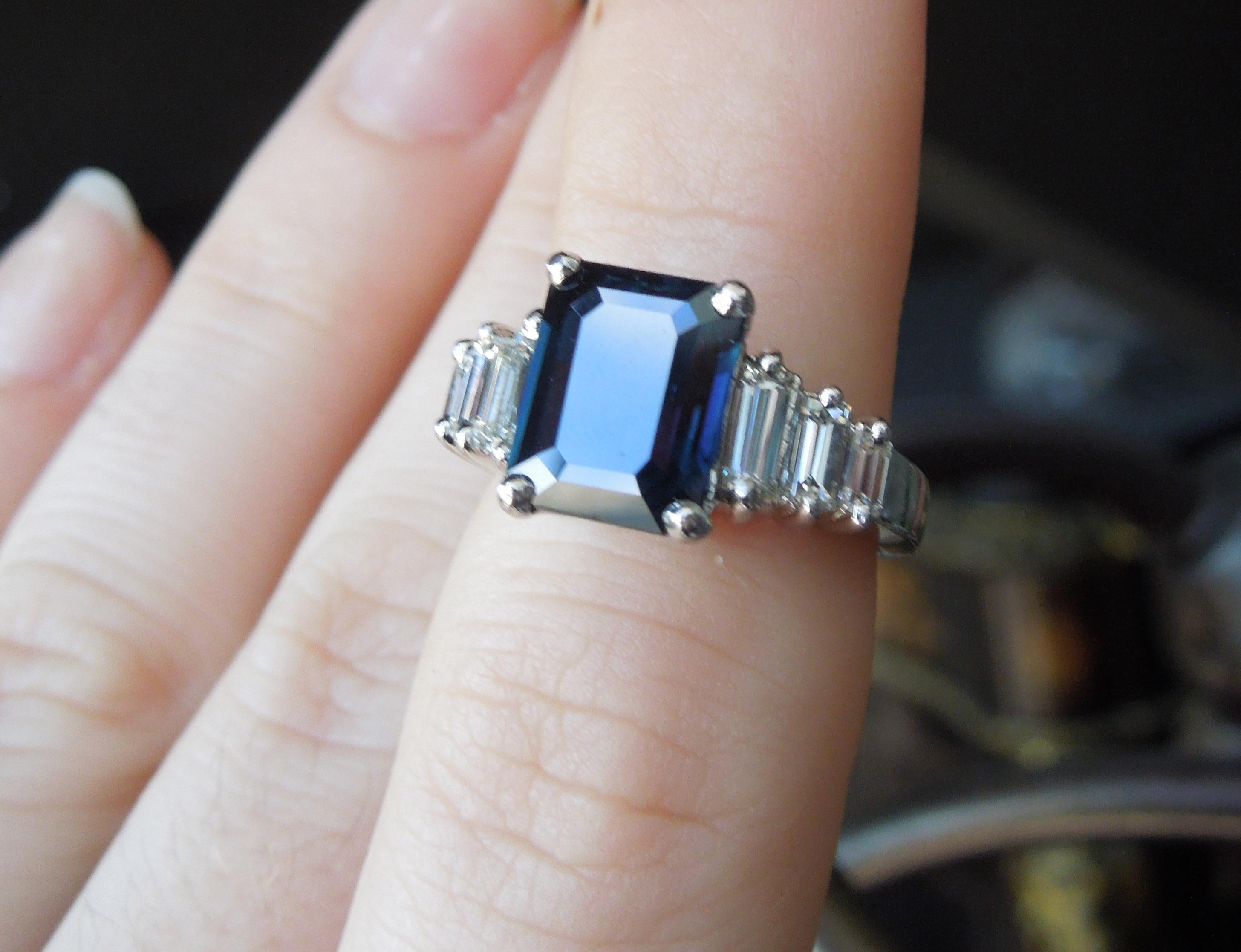 Featuring a central 4 carat Emerald cut Blue Sapphire, with a slight Green tinge, at 9.5mm in length x 7.5mm in width, secured in a 4-Prong setting. With a total of approximately 0.90 carats of Colorless Nearly Flawless Rectangular Baguette cut