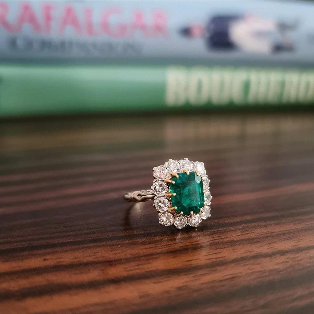 An exquisite and fine quality emerald and diamond cluster ring from France. French assay marks. Central emerald-cut Colombian emerald of approximately 2.75 carats mounted in 18-carat yellow gold claws, surrounded by 12 round-cut diamonds to form a