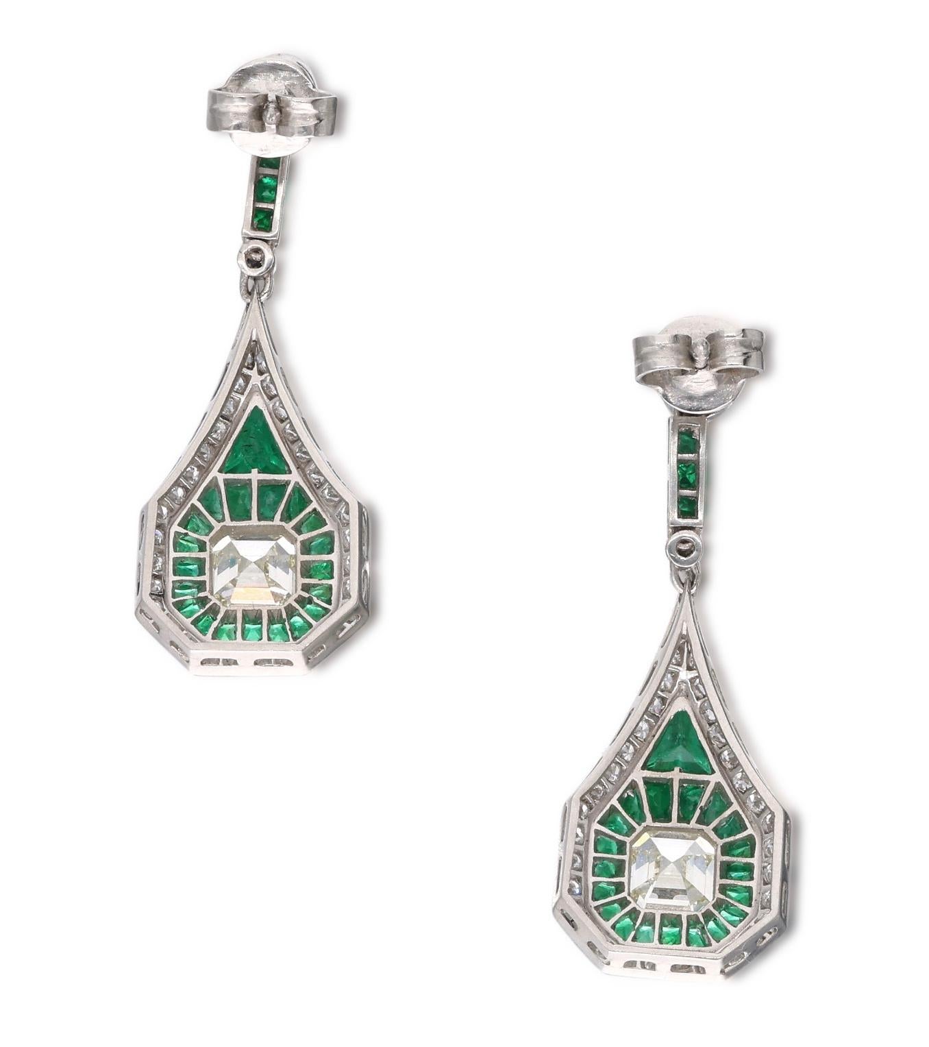 A pair of beautiful art deco inspired drop earrings that feature square emerald cut diamonds, which are accented by Old European cut diamonds and emeralds. The square emerald cut diamonds weigh a total of approximately 2 carats, and the Old European