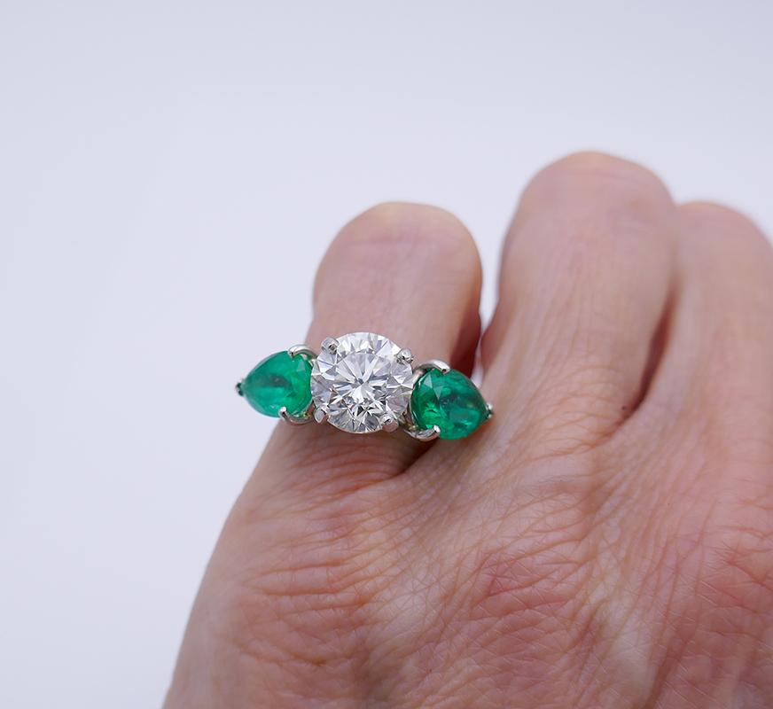 	A dazzling diamond emerald platinum ring. 
        This timeless ring has a classic three stone design often used for anniversary rings. For an anniversary ring, this design traditionally represents a couple’s past, present and future. The center