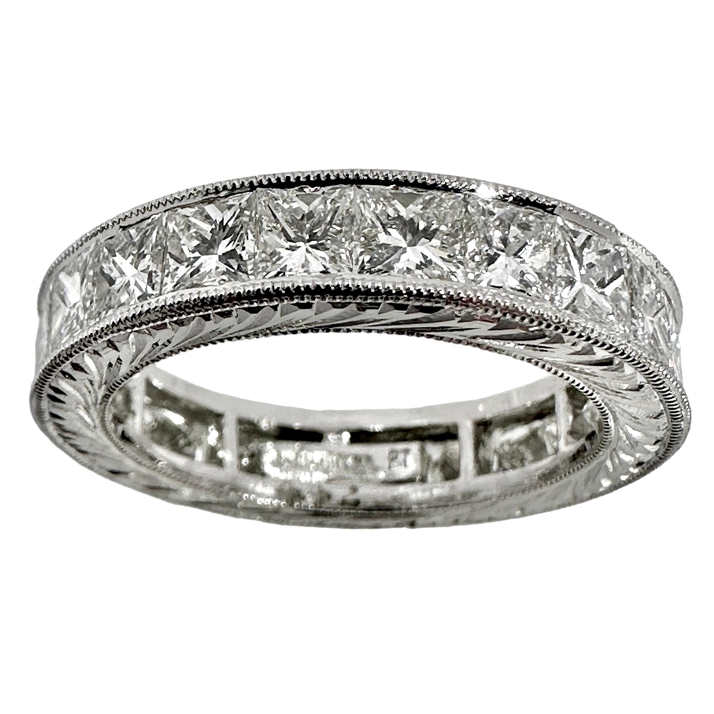 A classic eternity band set with twenty one princess cut diamonds in a platinum mounting. Each diamond weighs an average .21cts. 
This beautifully detailed ring has mill grained edges facing the front with fine quality engraving on the top and
