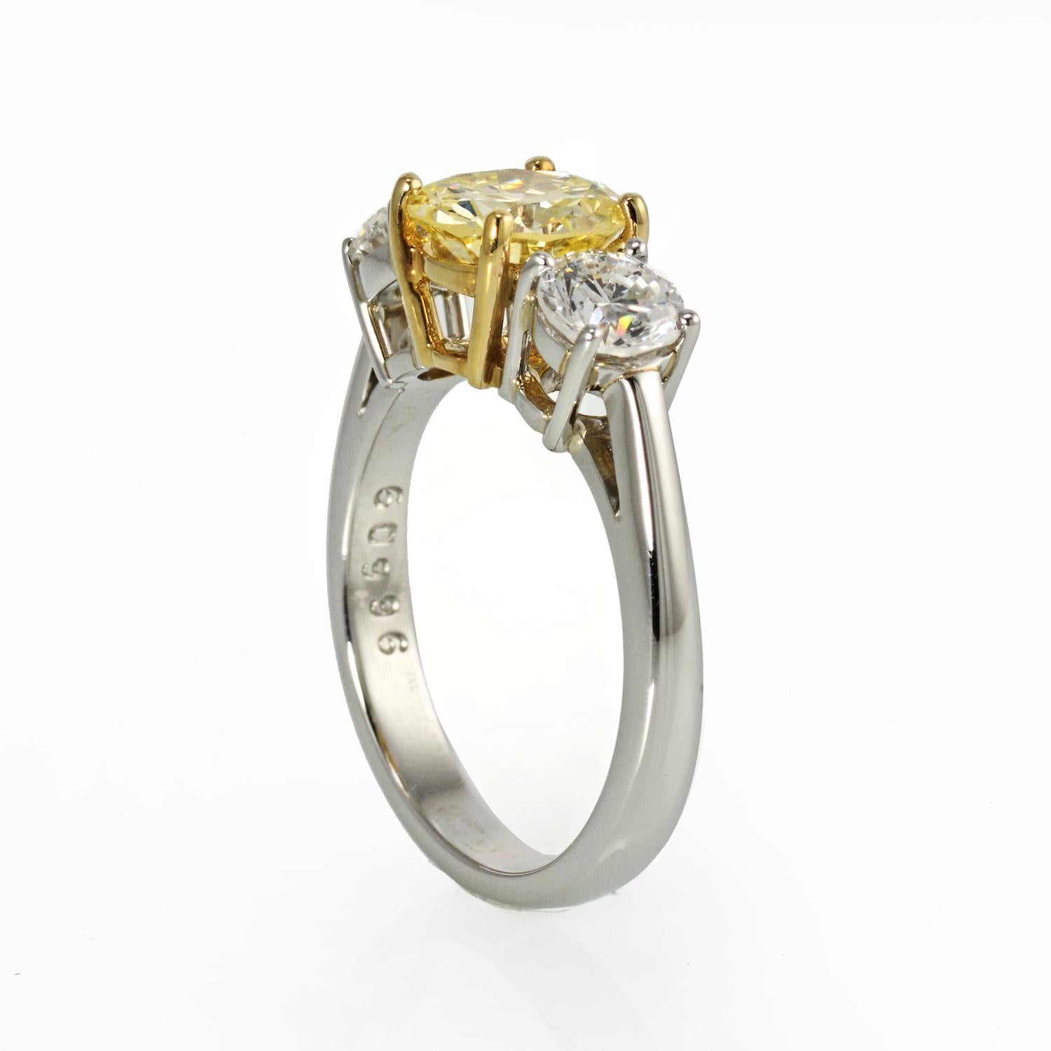 This 1.45 ct Natural Color Fancy Yellow center diamond is flanked by 2 colorless 1/4 ct round diamonds. The diamonds are set in a hand-crafted Platinum & 18 Yellow gold mounting.  The center Fancy Yellow diamond is set into a 18K yellow gold basket