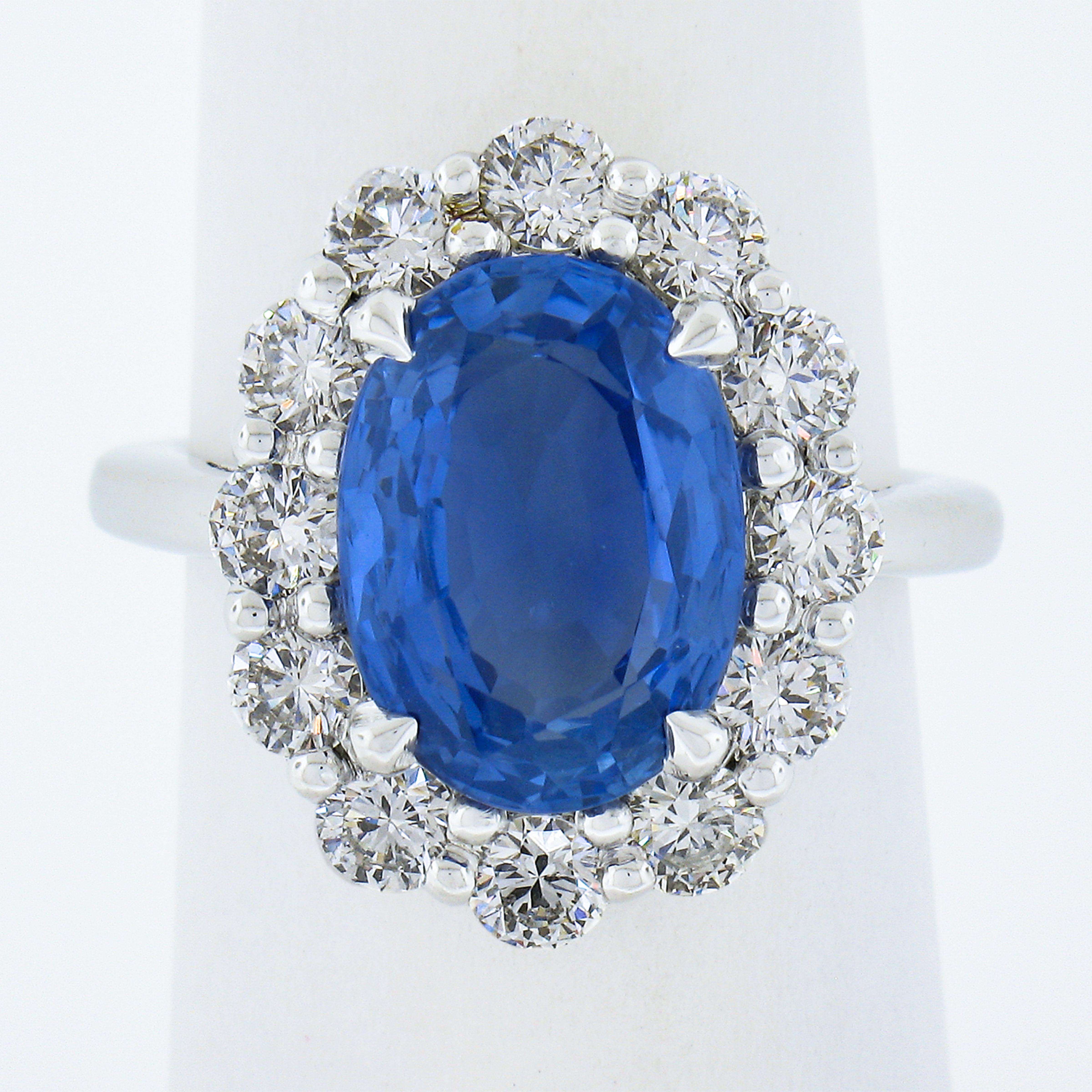 This brand new sapphire and diamond Princess Diana engagement/cocktail ring is crafted in solid platinum and features a stunning 6.08 carats of the most wonderful cornflower blue imaginable with a classic and perfectly proportioned oval cut. It