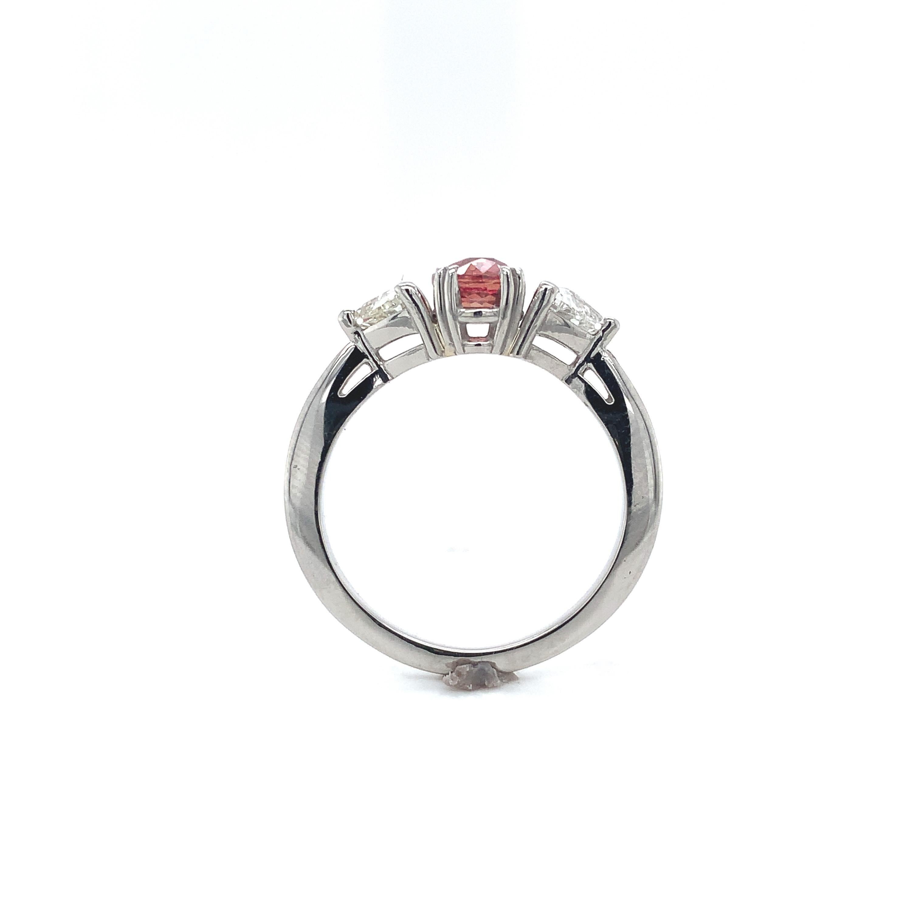 Platinum 3 stone ring featuring an oval natural padparadscha sapphire weighing 1.03 carats and diamonds. GIA report #2225462800 states natural sapphire measuring 6.62mm x 5.28 x 3035mm, stating pinkish orange color (with no other modifiers). The
