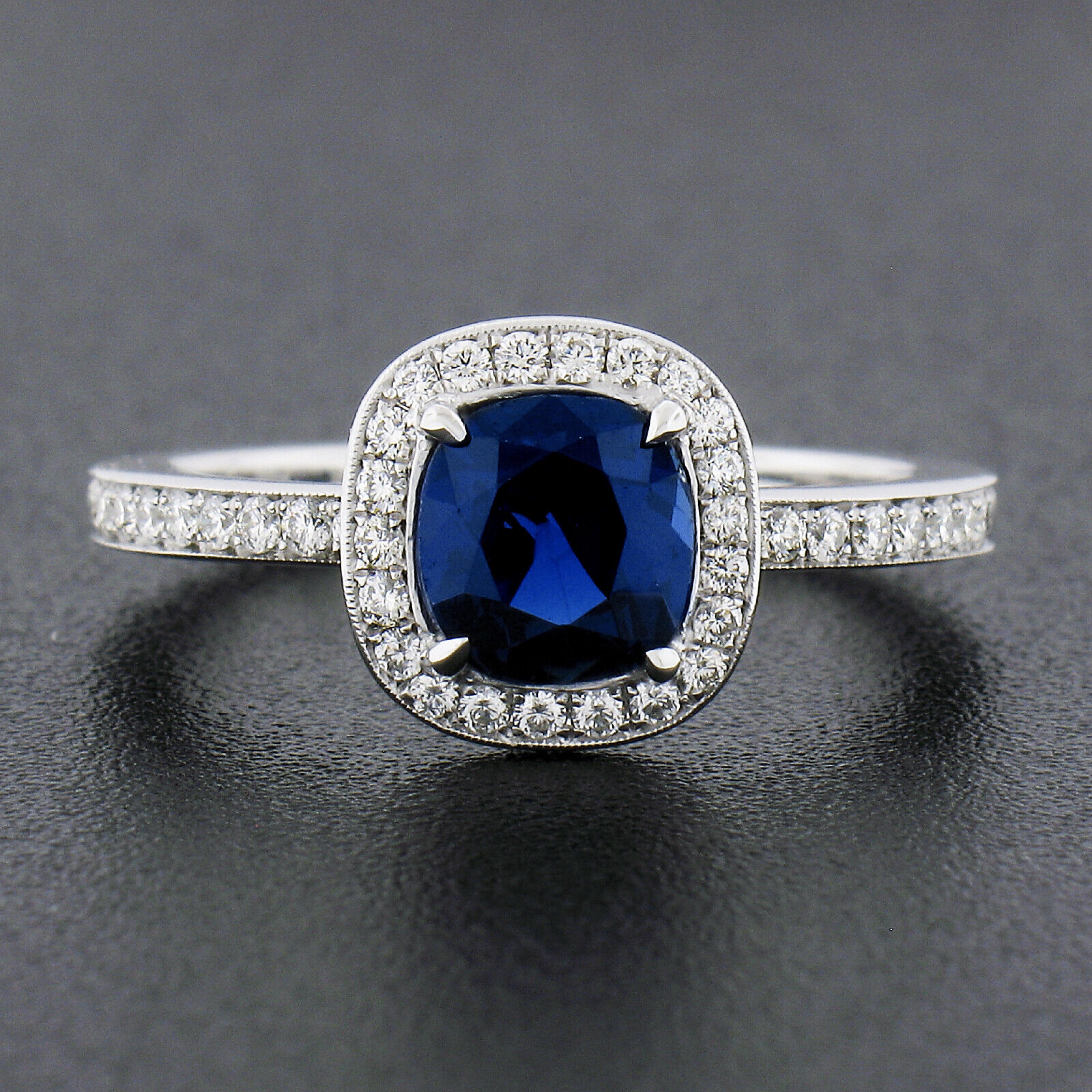 This gorgeous and fiery sapphire and diamond ring was crafted in solid platinum and features a stunning, GIA certified, natural genuine sapphire solitaire neatly prong set at the center of a brilliant diamond halo. This cushion cut sapphire has a