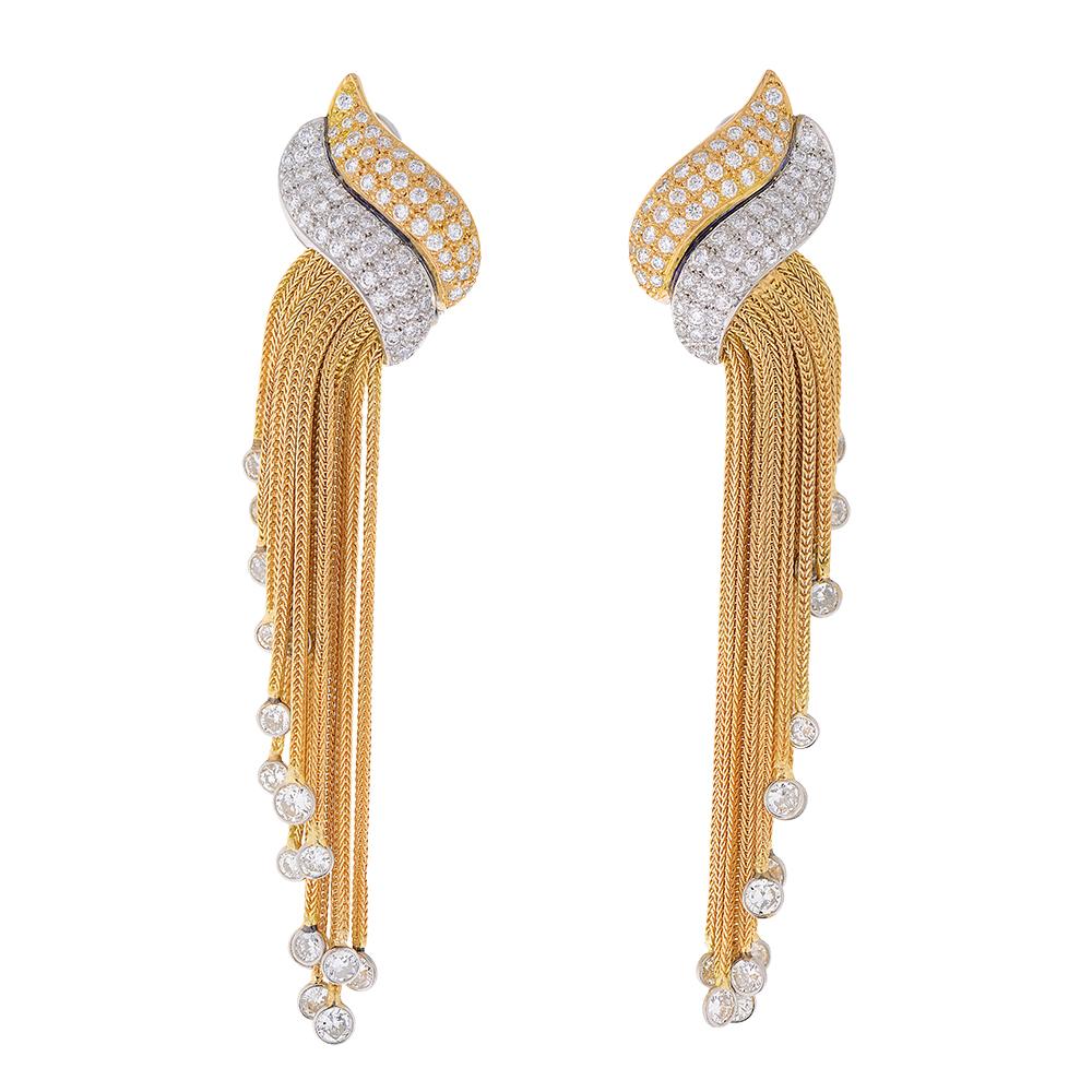A pair of stylish mid-century style diamond earrings. Designed as cascading waterfall of yellow gold chains, each concluded with a round diamond in a platinum surround. Suspended from a platinum and gold stylised ribbon pavé-set with brilliant-cut