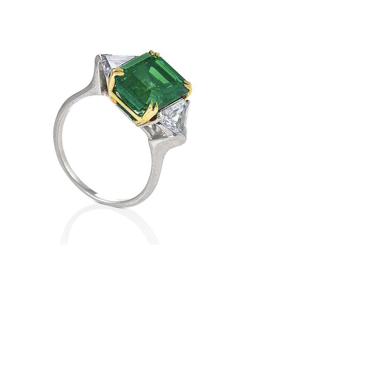 A platinum, 18 karat gold, emerald and diamond ring.  The ring centers on an emerald-cut Colombian emerald weighing 5.56 carats, flanked by 2 triangular-cut diamonds with an approximate total weight of 1.70 carats. Accompanied by  American