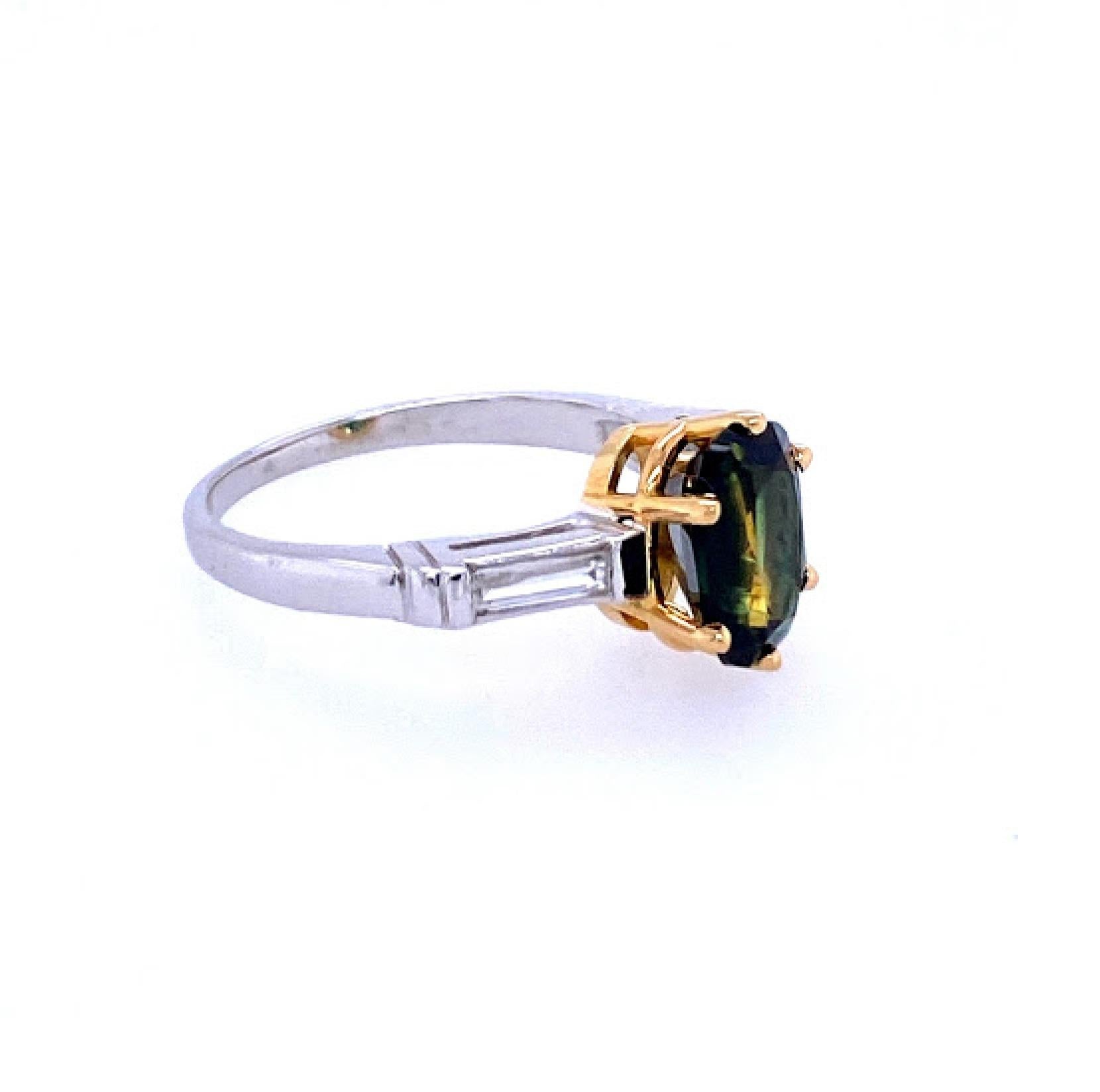 Platinum (stamped 10%IRID PLAT) ring featuring 8.85 mm by 6.9 mm oval green sapphire weighing 2.74 carat, set in a 18 karat yellow gold 6 prong basket head. The center stone is flanked by two 5.5 mm by 2.5 mm straight baguette diamonds weighing 0.12