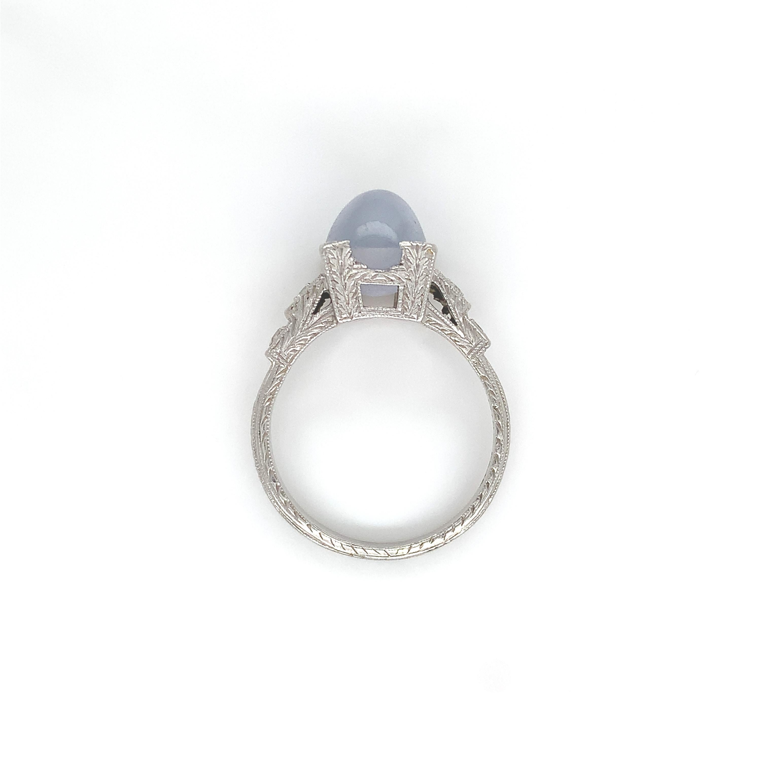 Platinum ring featuring a light blue/gray cabochon star sapphire. The sapphire measures about 8.7mm x 7.2mm. There are 4 small round diamond accents, 2 measuring about 1.8mm and 2 about 1.5mm. The platinum setting is hand engraved on 3 sides and