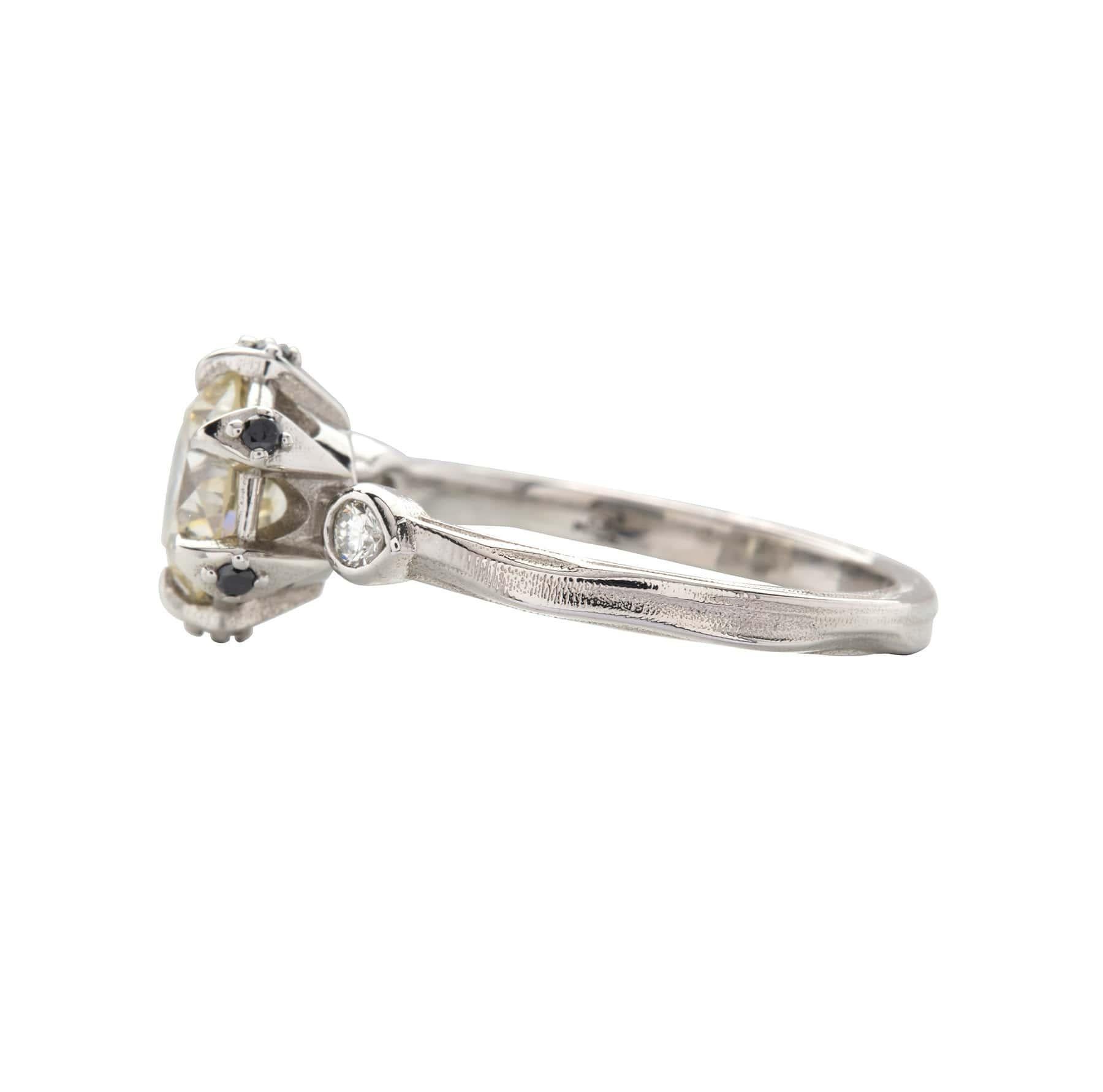 A one-of-a-kind GIA-certified 7mm Old European Style Round Brilliant Cut Diamond with amazing VVS1 clarity has a subtle hue of color, graded O-P.  This center stone is set in a platinum setting that forms the shape of a crown with 6 black