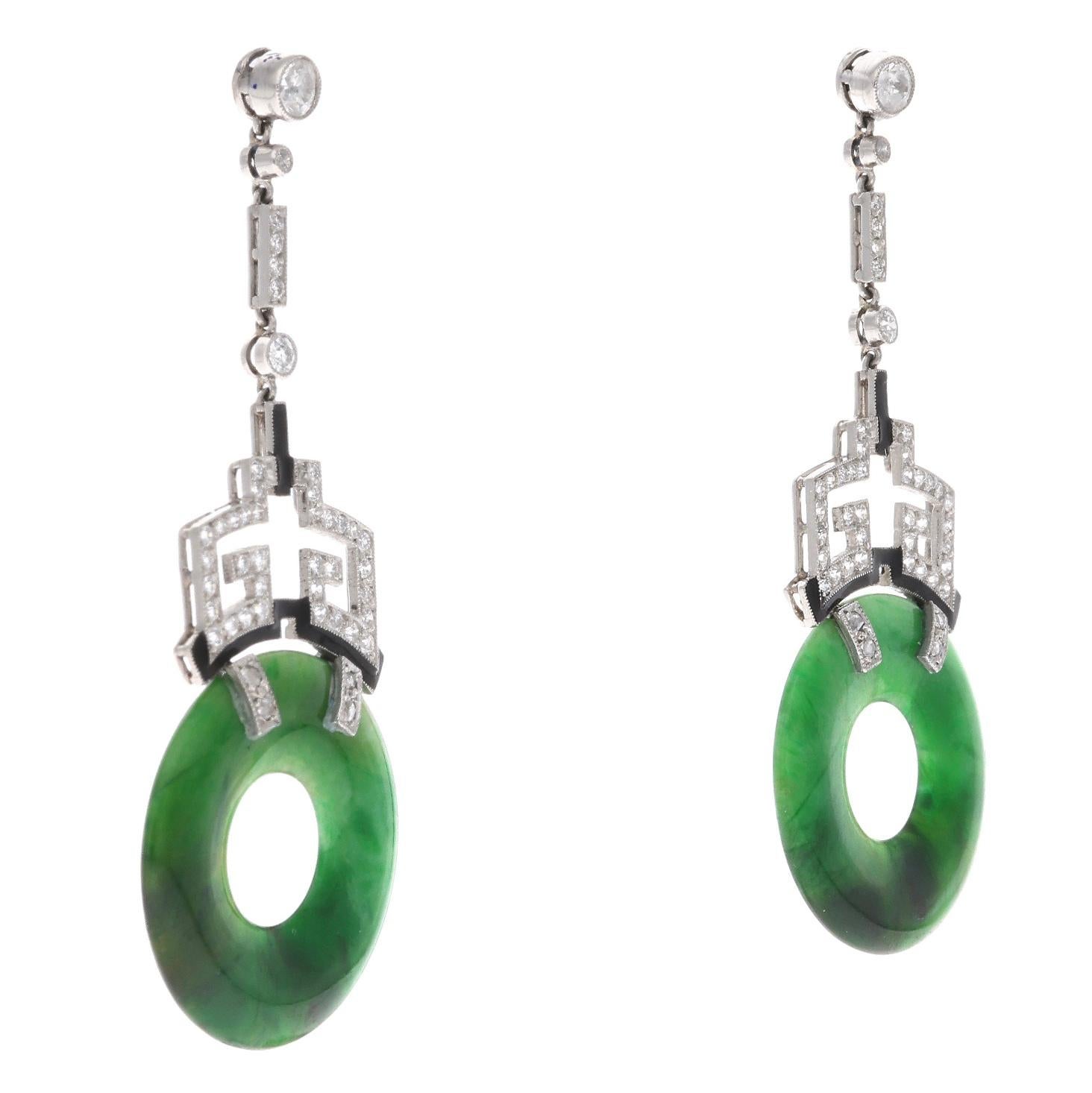 A pair of art deco earrings that feature jadeite rings. These rings are suspended from diamonds and enamel accented drops. The diamonds weigh a total of approximately 1 carat and are set on platinum. Total weight: 11.60 grams. Length: 2 inches. 
