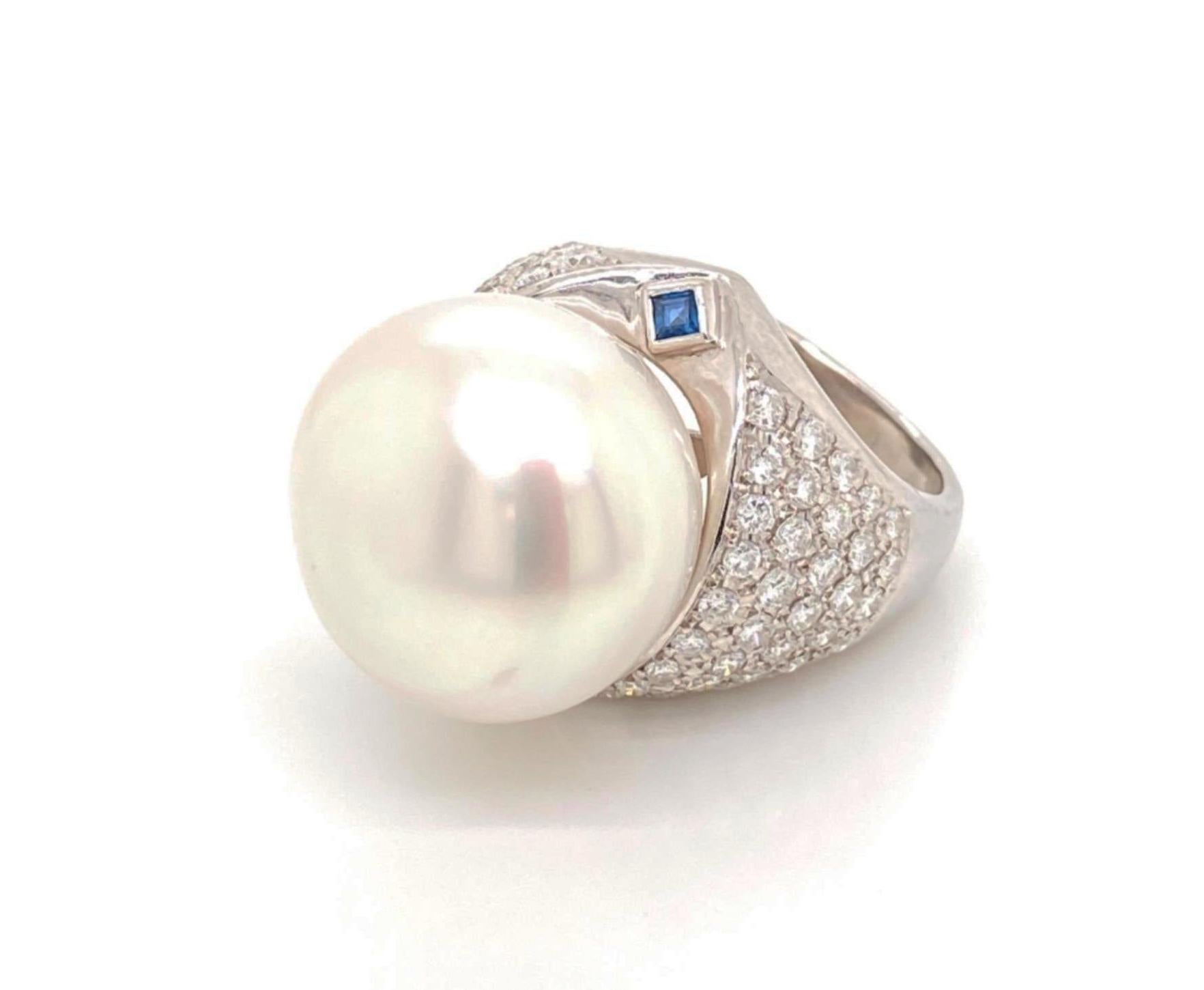 This is an eye catching impressive ring, it is crafted from 18k white gold featuring a large 18.3mm shimmering pearl sitting on top of a wide dome form with round cut diamonds, on each side of the top of the shank is a square cut bezel set sapphire