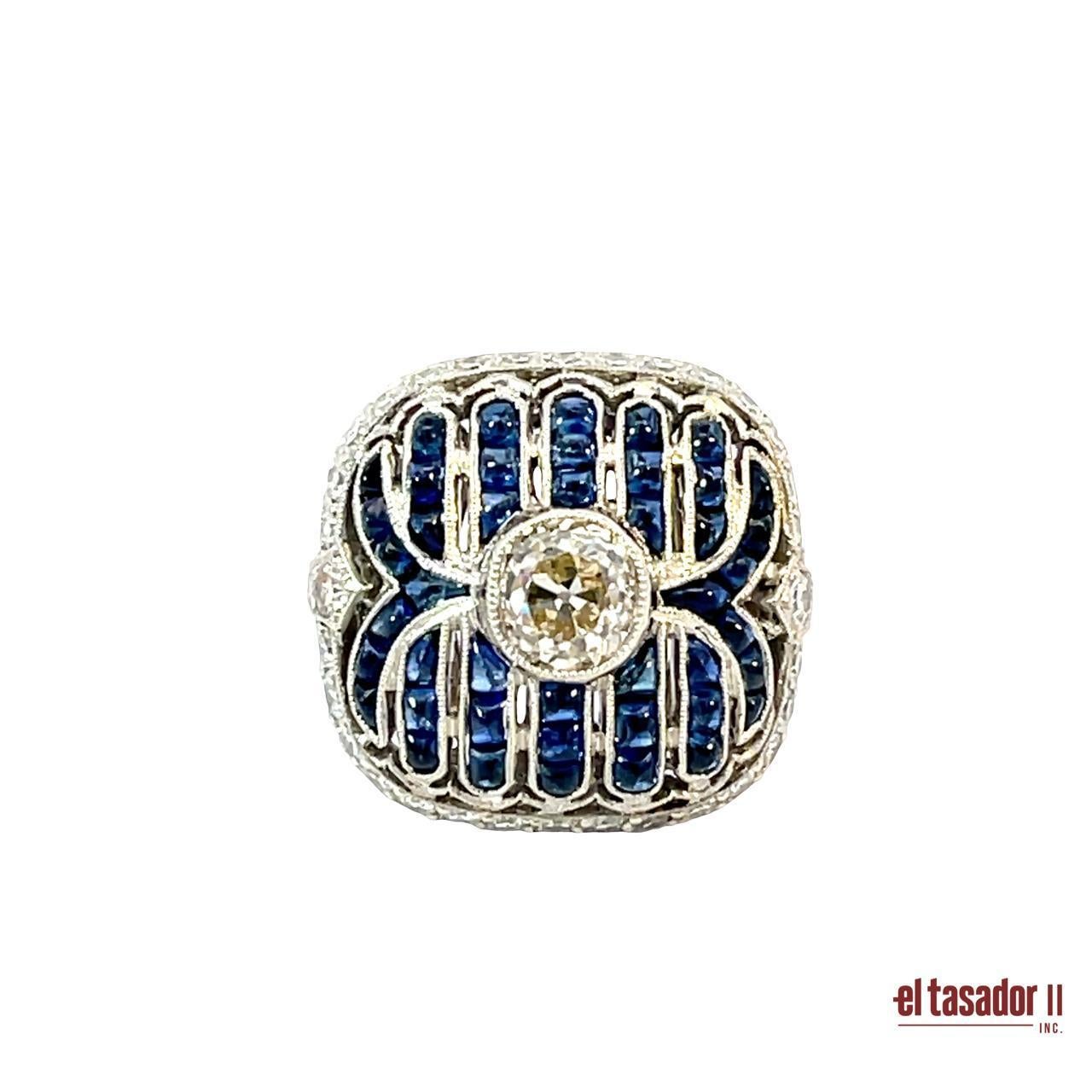 A bold and captivating statement piece, this platinum ring showcases a 0.96-carat brilliant-cut diamond at its center, bezel-set and framed by 0.75 carats of additional diamonds. Rich blue sapphires totaling 3.73 carats are meticulously channel-set